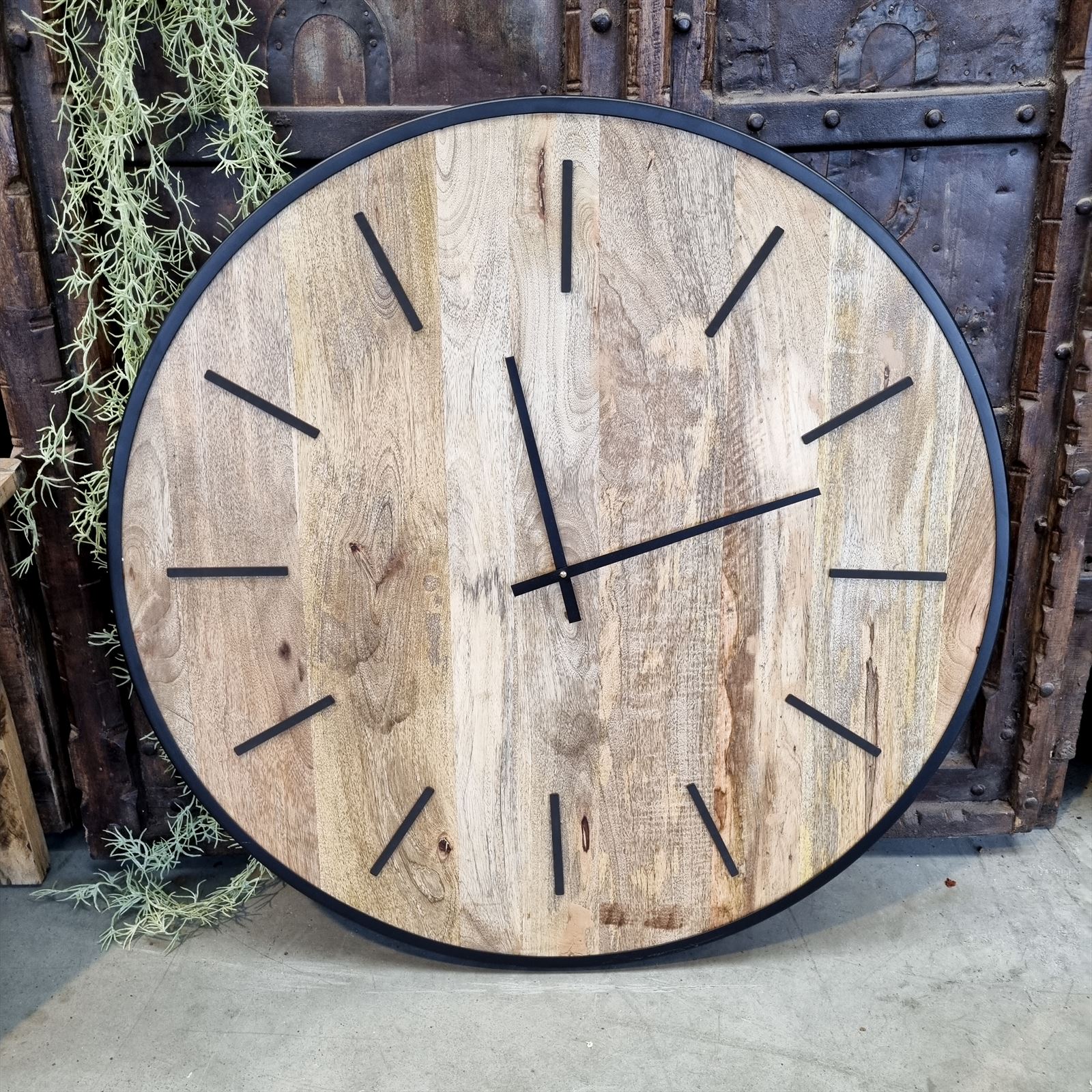 Große Wanduhr Mango mit schwarzen Zeigern und Strichen als Stundenmarkierungen, auf einem Betonboden stehend - Benoa