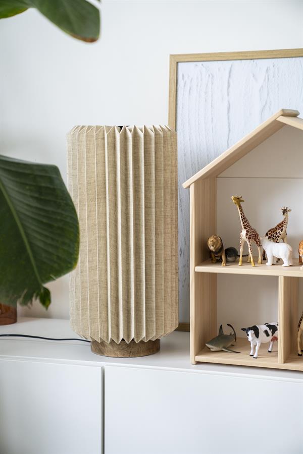 Tischleuchte Zuki mit plissiertem Stoffschirm auf einer weißen Kommode neben einem Holzpuppenhaus mit Spielzeugtieren - By-Boo