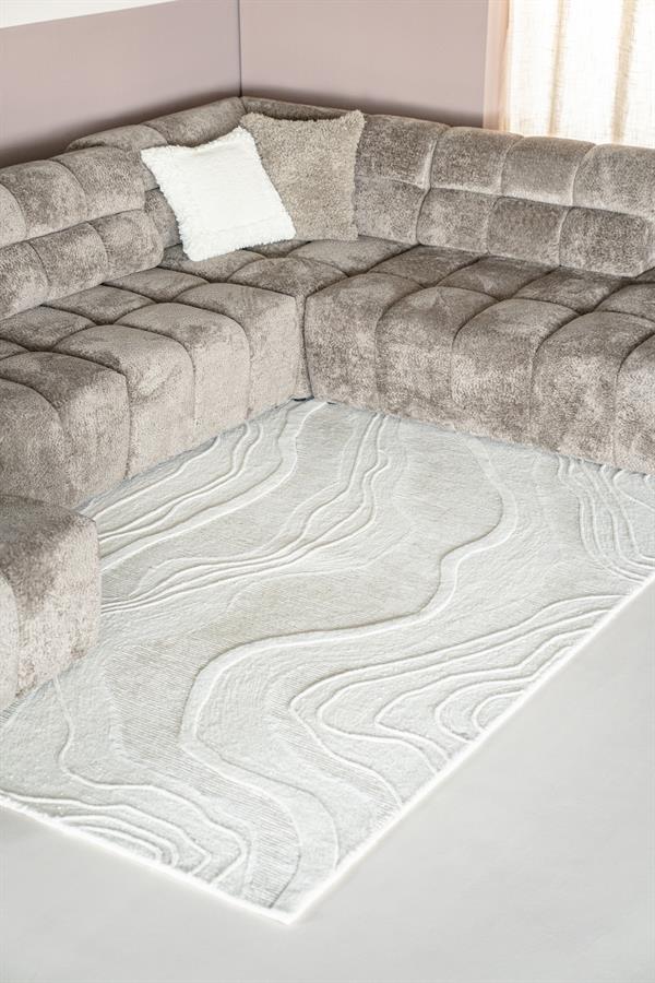 Teppich Soil mit wellenförmigem Muster auf dem Boden vor einem grauen Ecksofa - By-Boo