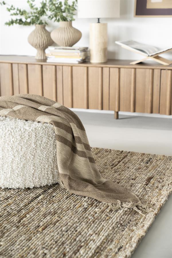 Decke Linje mit braunen und beigen Streifen, drapiert über einem weißen Pouf auf einem Juteteppich - By-Boo