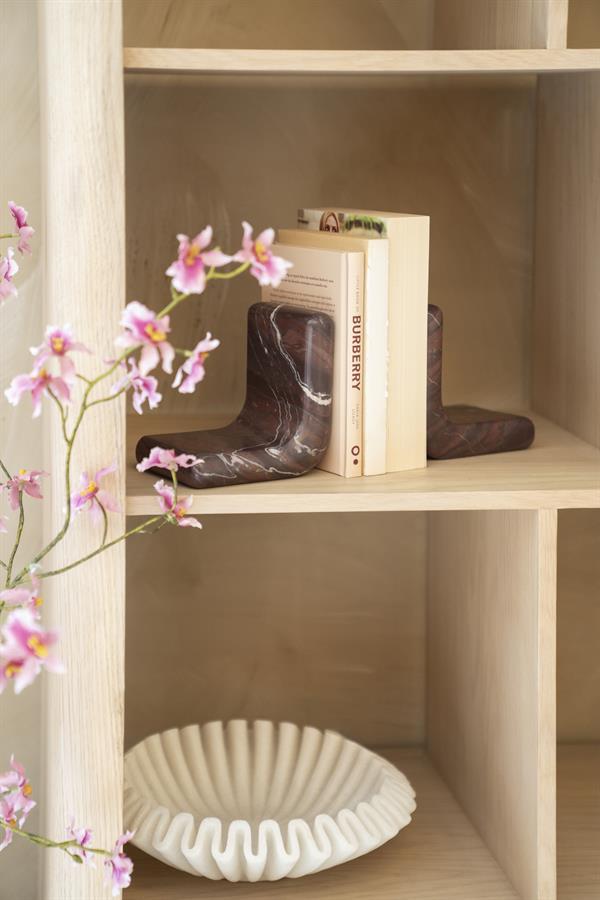 Die Buchstütze Rosso hält Bücher auf einem hellen Holzregal, mit rosa Orchideen im Vordergrund - By-Boo