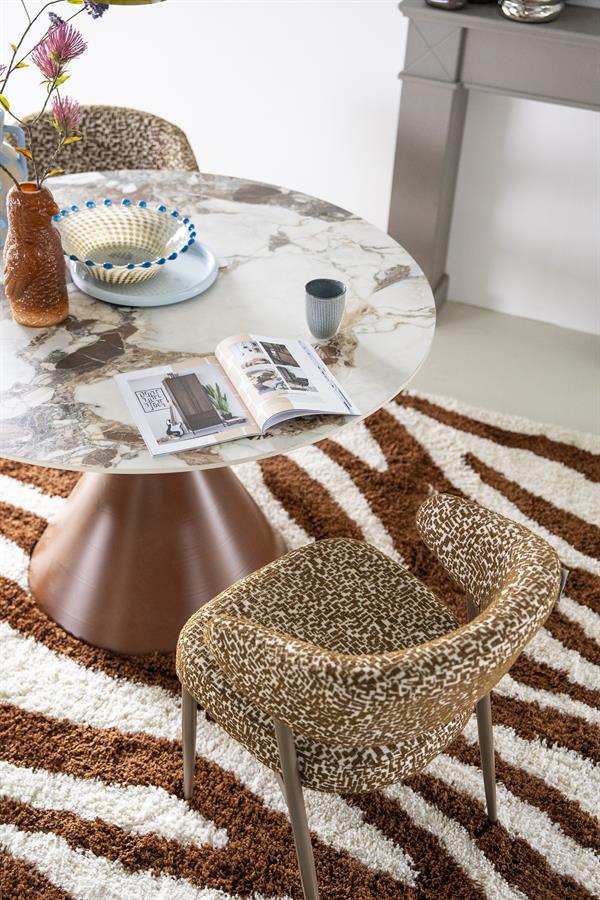 Der Esstisch Roka mit Marmorplatte und braunem Fuß, umgeben von Stühlen mit Leopardenmuster auf einem Zebra-Teppich - By-Boo