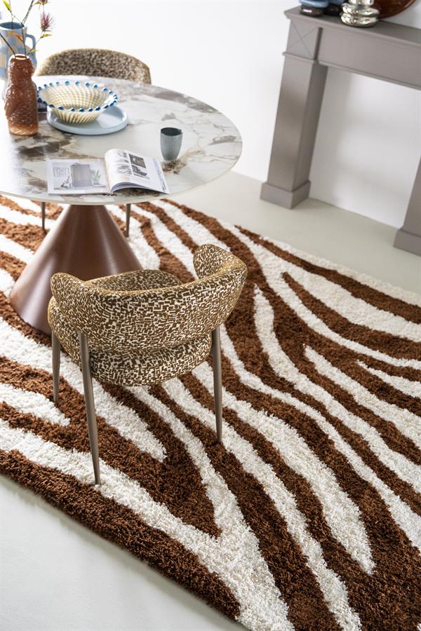 Teppich Marty Caramel mit Zebradruck in Braun und Weiß unter einem runden Esstisch mit Stühlen - By-Boo