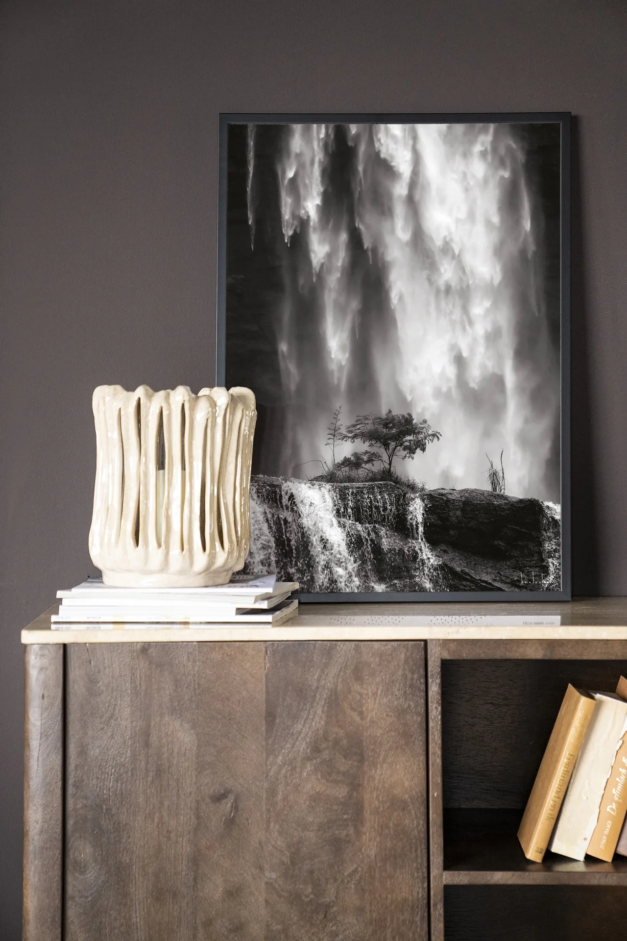 Wandkleed Germinate - Urban Cotton hangt boven een houten dressoir met een vaas en boeken