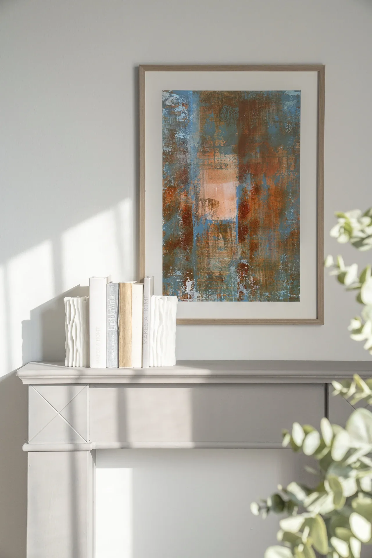 Der Art Print Blue Ocker Abstract 2 - Urban Cotton hängt über einem hellen Kaminsims mit Büchern und Vasen