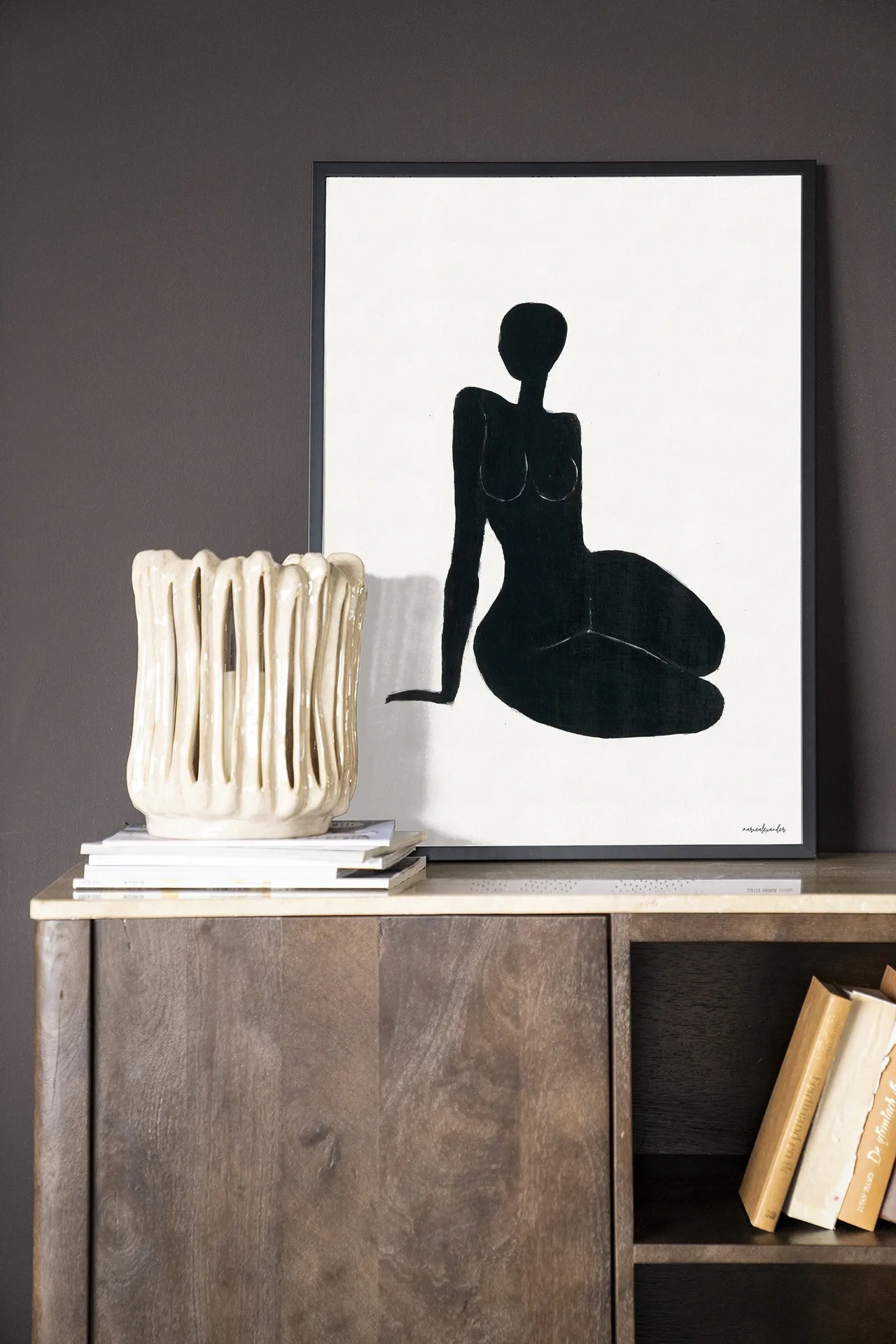 Een Art print International Woman - Urban Cotton in een zwarte lijst, leunend op een houten dressoir met een marmeren blad