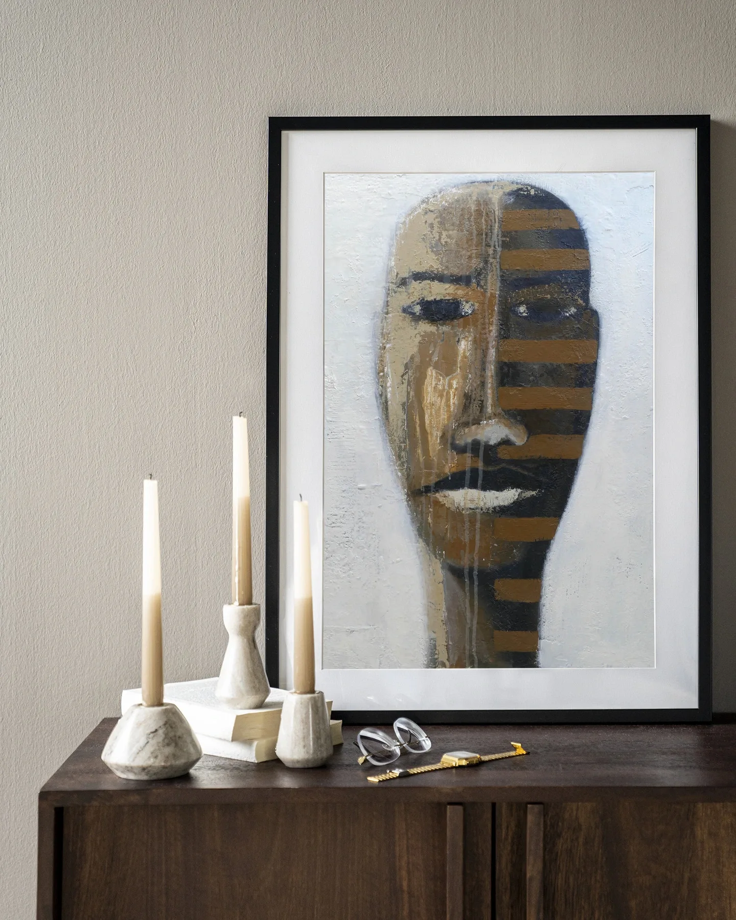 Wandteppich Head 1 - Urban Cotton hängt in einem schwarzen Rahmen über einem dunkelbraunen Schrank mit Kerzen