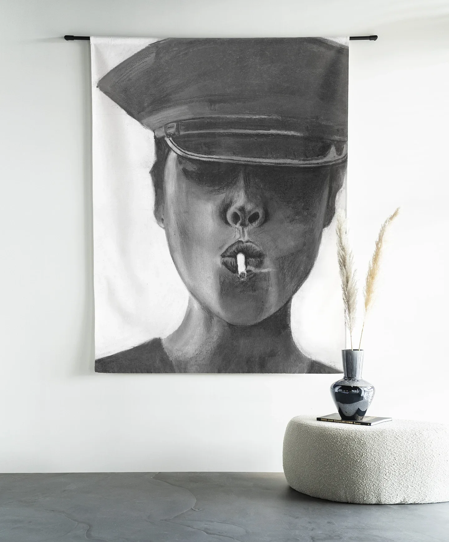 Wandteppich Smokes - Urban Cotton hängt an einer schwarzen Stange über einem weißen Pouf mit einer Vase