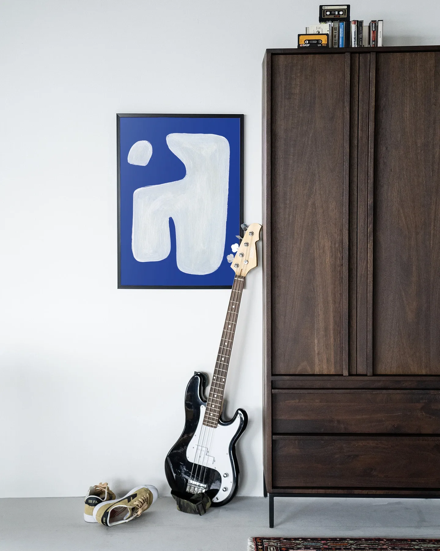 Wandteppich Pacman - Urban Cotton hängt an einer weißen Wand neben einem dunkelbraunen Schrank mit einer Bassgitarre davor