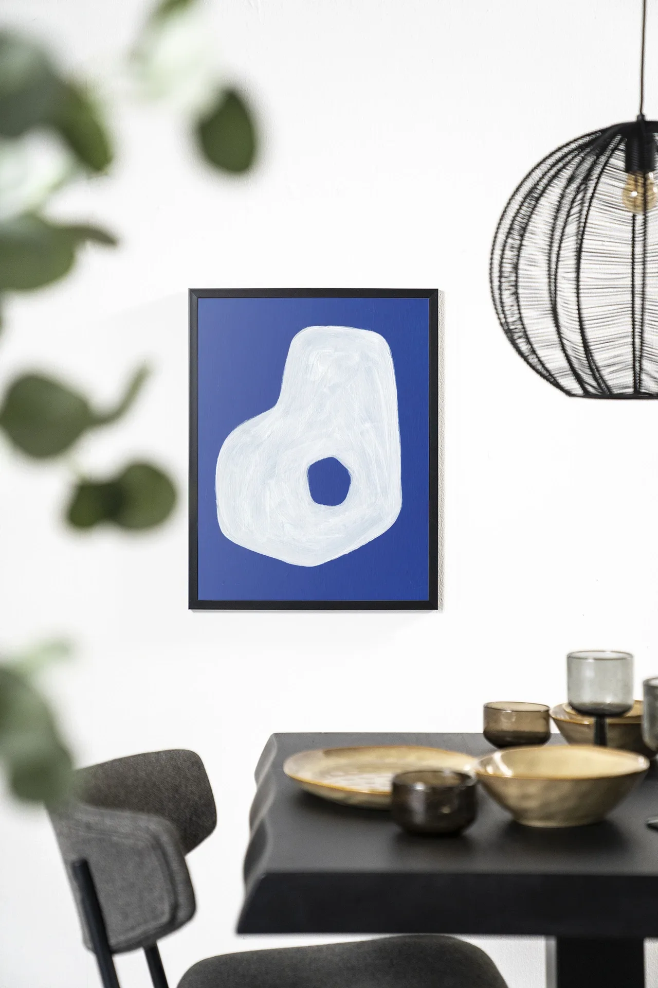 Wandkleed Spook - Urban Cotton hangt aan een witte muur boven een zwarte eettafel met gouden schalen