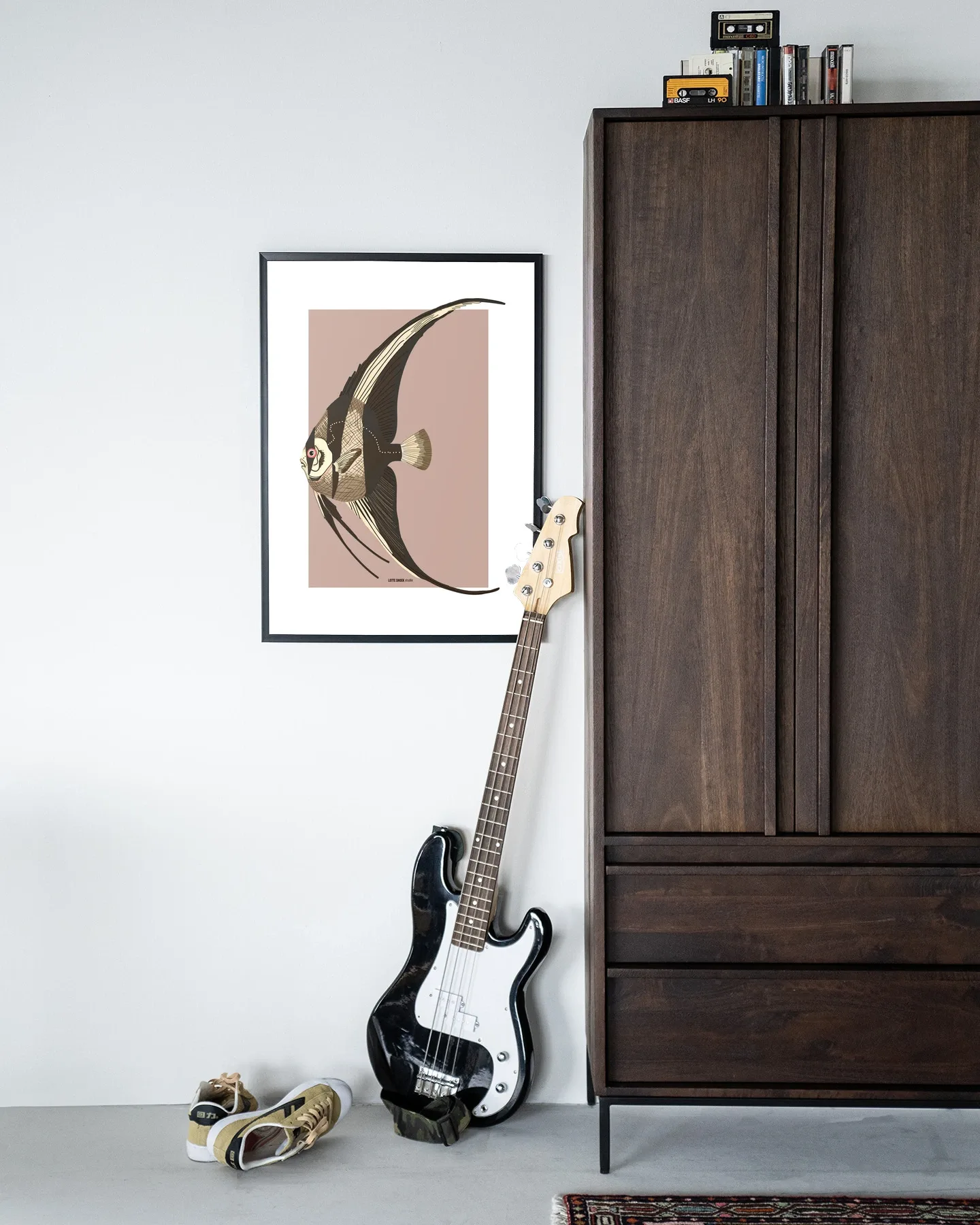 De Art print Mola Mola - Urban Cotton hangt aan een witte muur naast een donkerbruine kast met een basgitaar ervoor