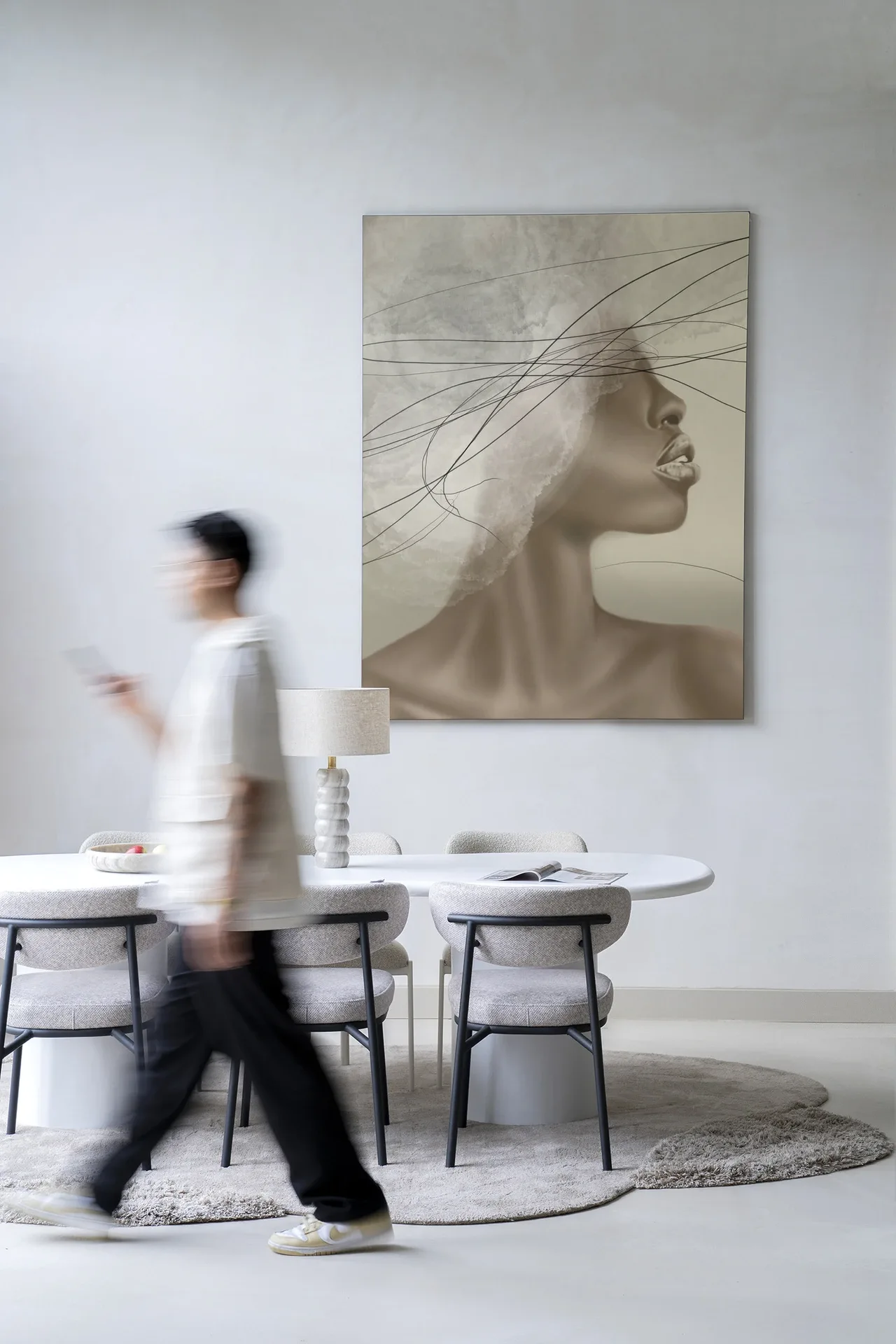 Een wazige persoon loopt langs een witte eettafel met stoelen en het wandkleed Cloudy thoughts - Urban Cotton