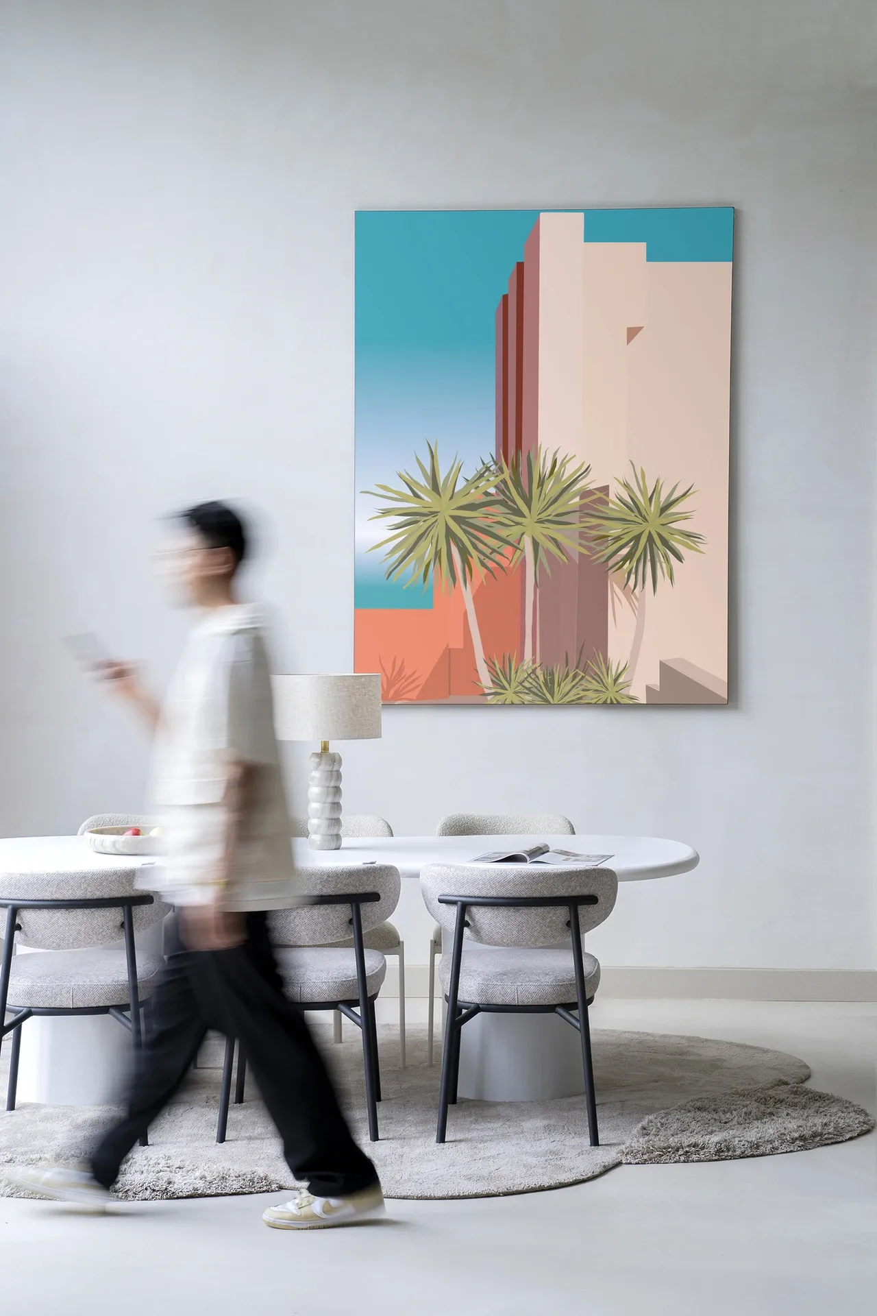 Wandkleed Tropical Place - Urban Cotton hangend aan een lichte muur boven een eettafel met stoelen, met een persoon die voorbij loopt