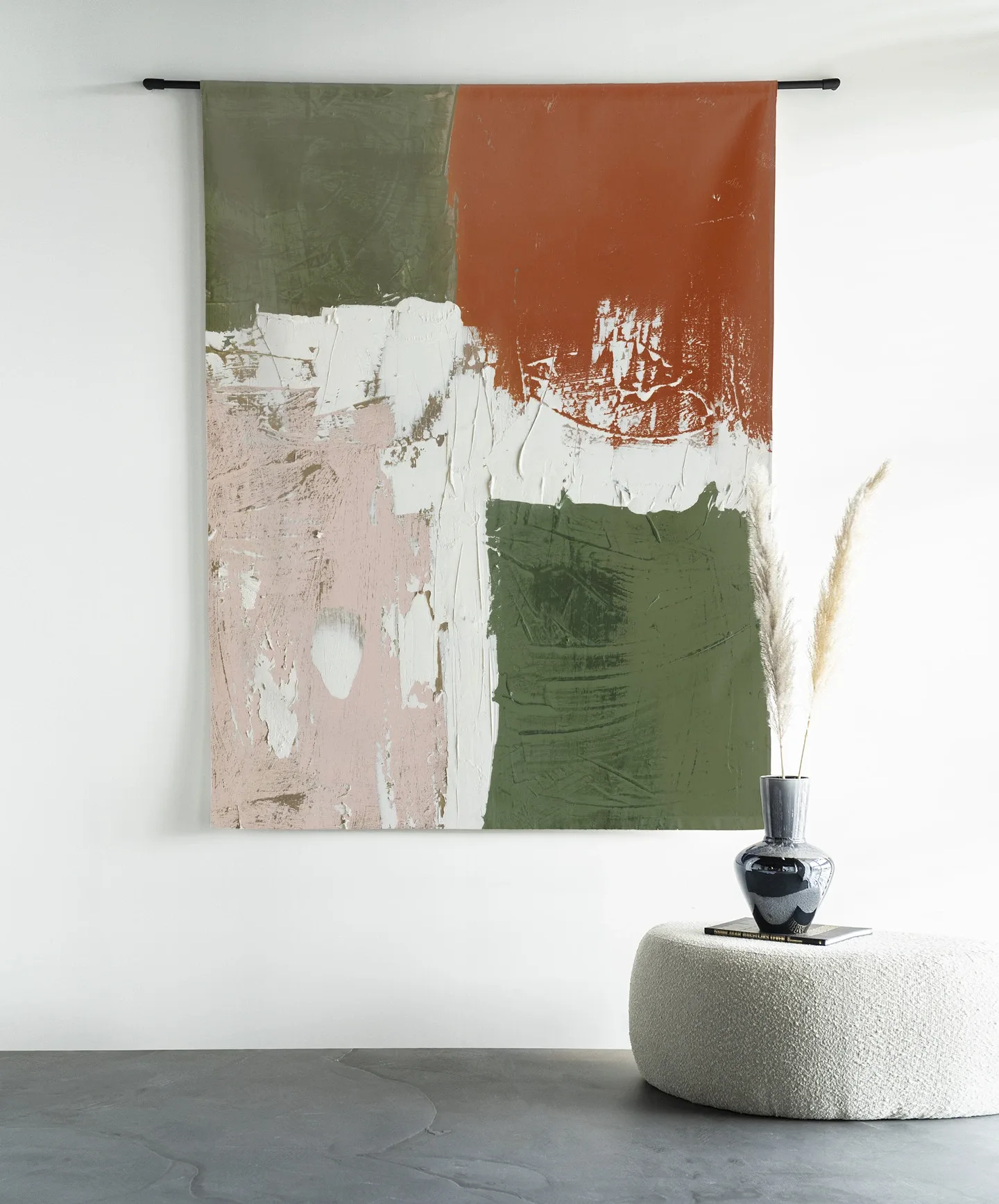 Wandteppich Artistic Chaos - Urban Cotton hängt an einer schwarzen Stange über einem runden Pouf mit einer Vase und Pampasgras
