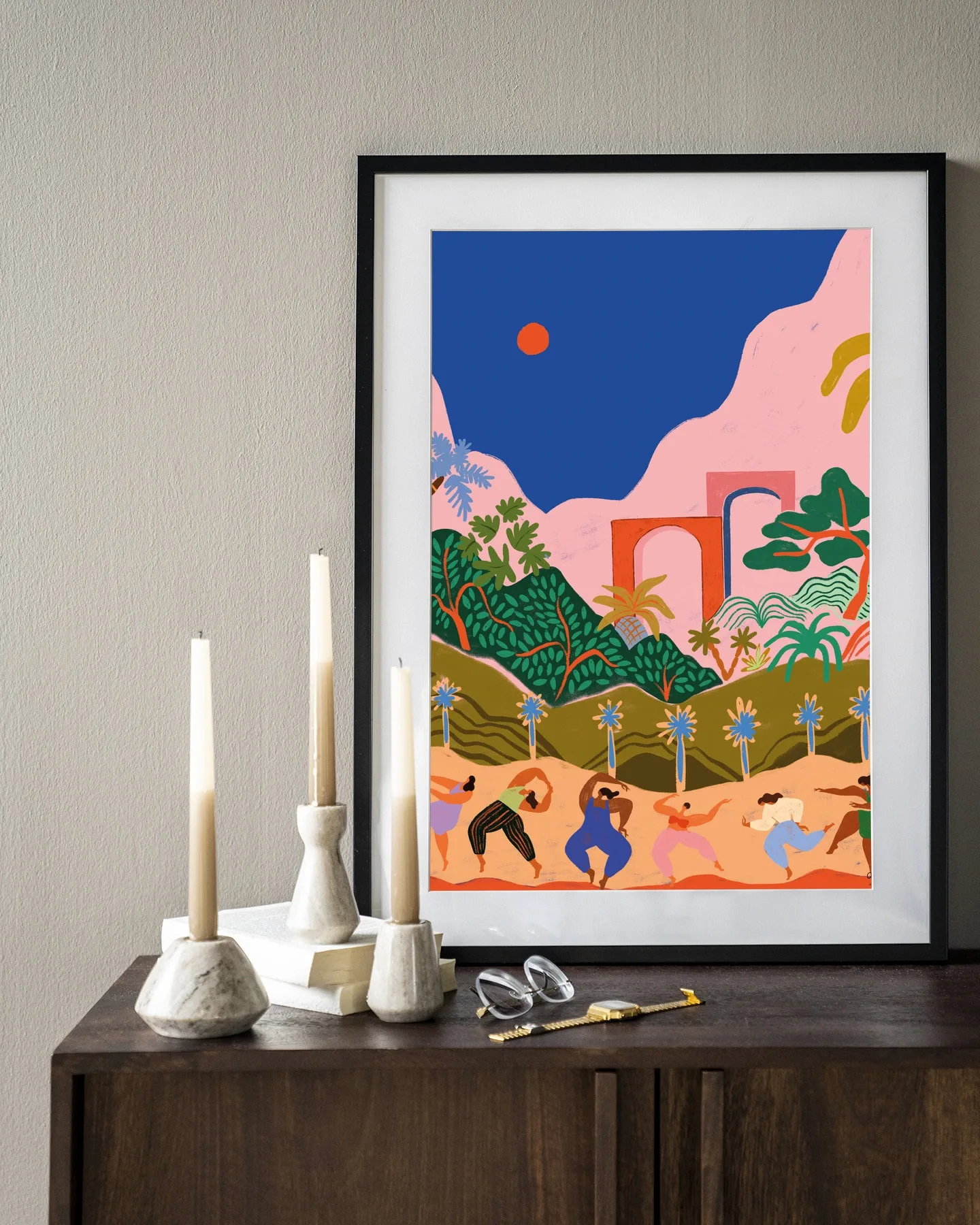 Wandkleed Dancing In Paradise - Urban Cotton in een zwarte lijst, staand op een donkerbruin dressoir met kaarsen en boeken