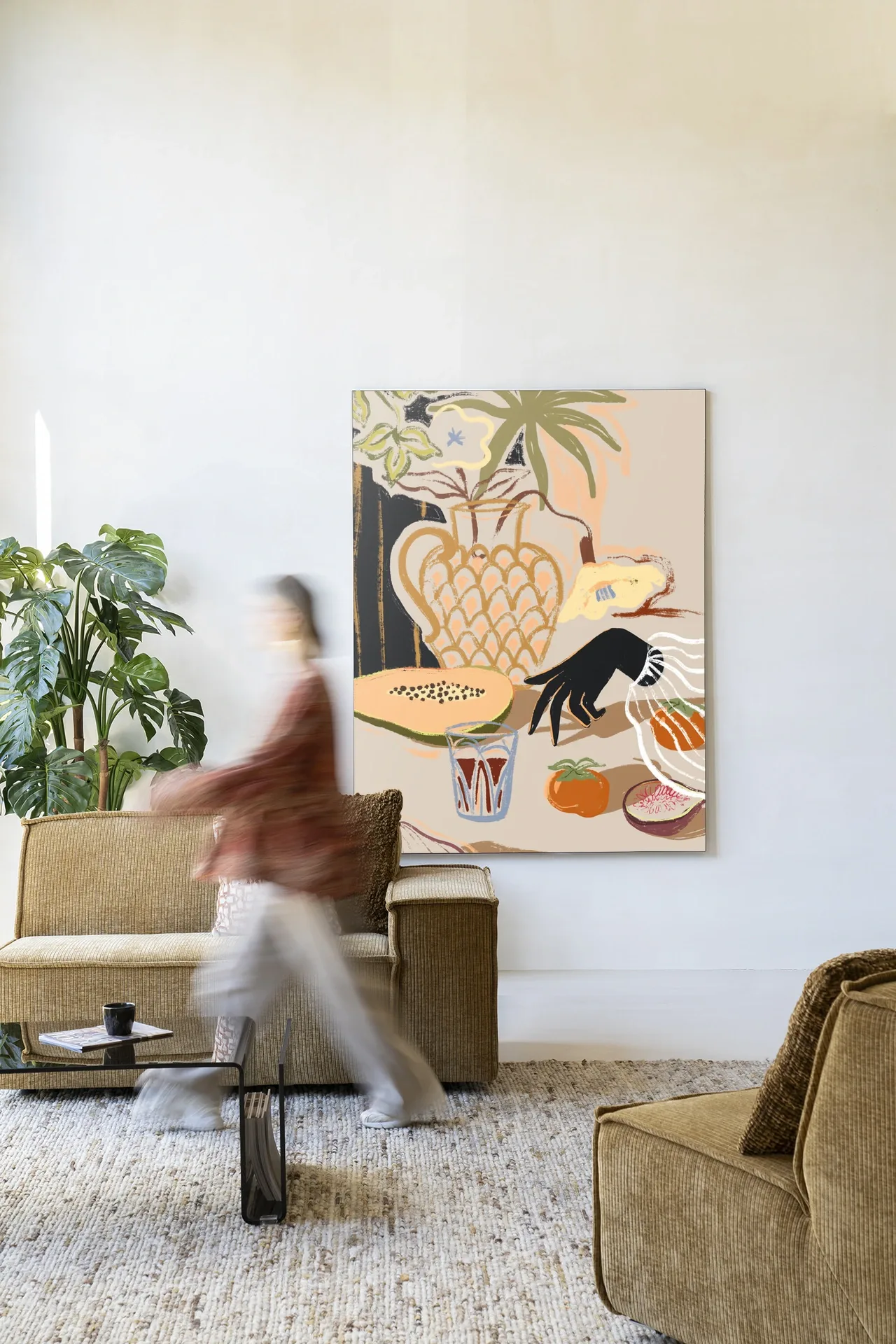 Wandkleed Fruitful Spread - Urban Cotton hangt aan een witte muur in een lichte woonkamer met een bank en salontafel