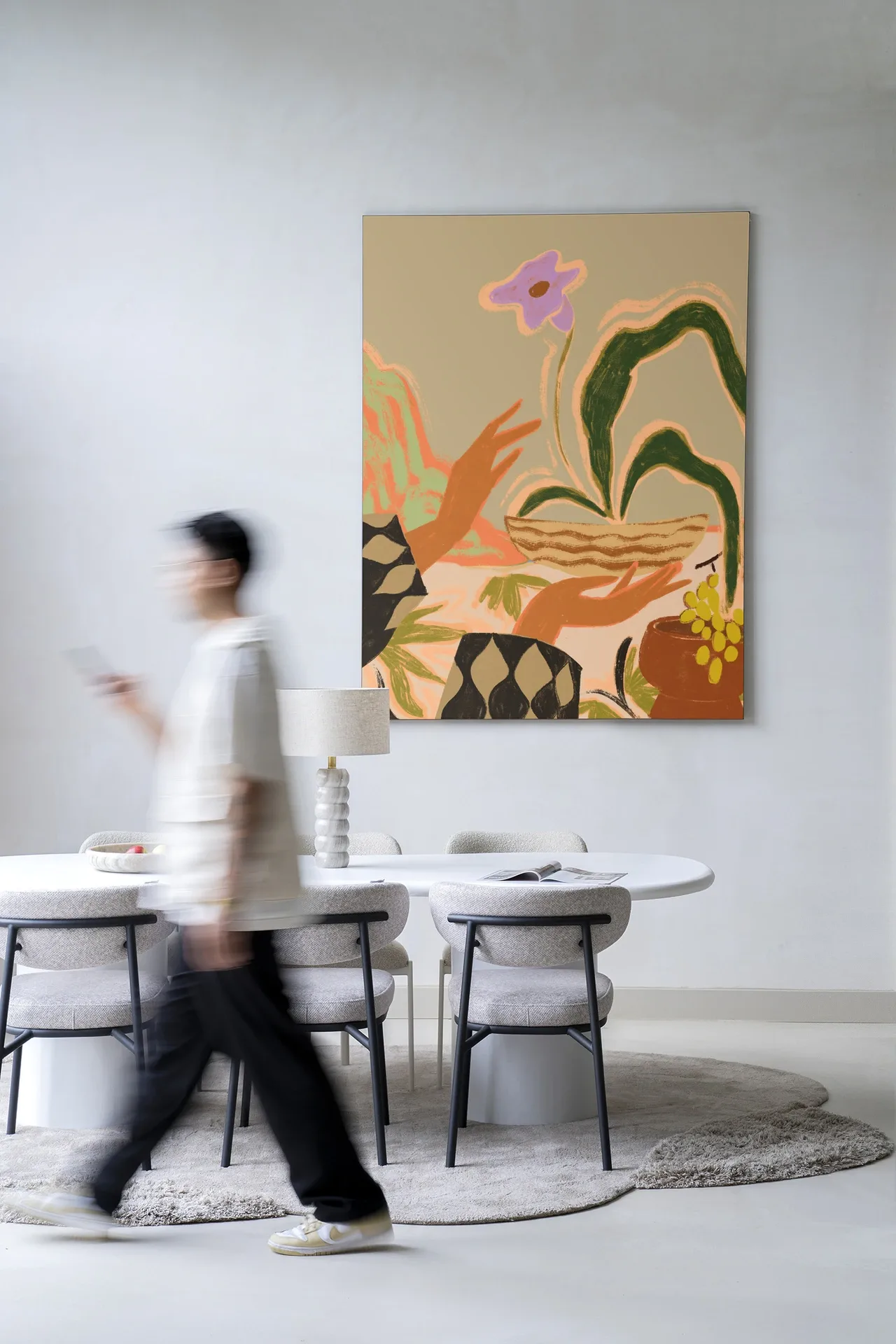 Een man loopt langs een eettafel met stoelen en een Wandkleed The Power of One - Urban Cotton aan de muur