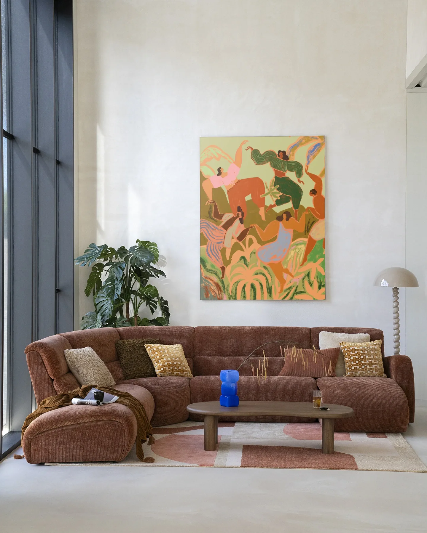 Een kleurrijk Wandkleed Spring Frolic - Urban Cotton hangt boven een bruine bank in een lichte woonkamer