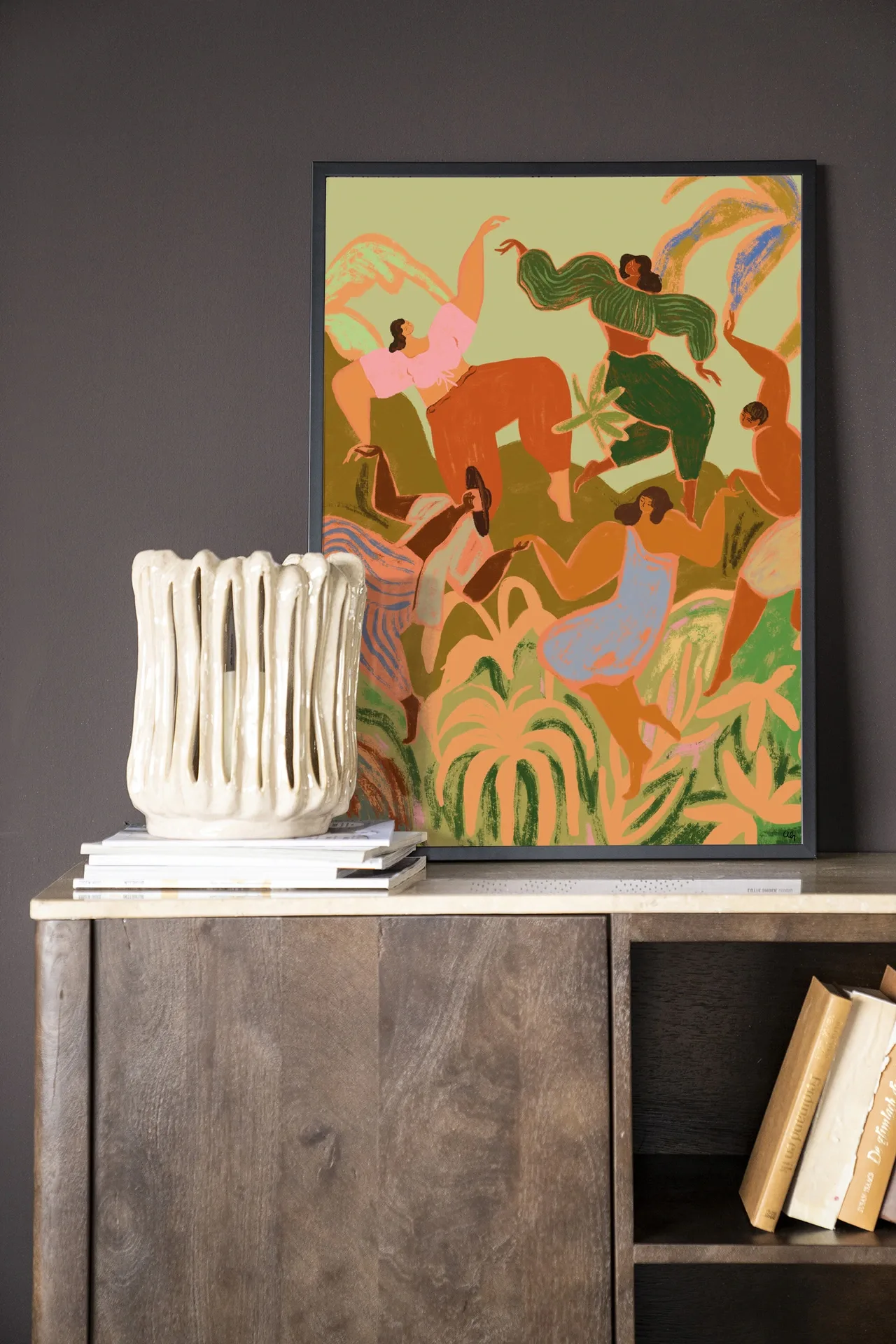 Wandkleed Spring Frolic - Urban Cotton hangt in een zwarte lijst boven een houten dressoir met een vaas en boeken