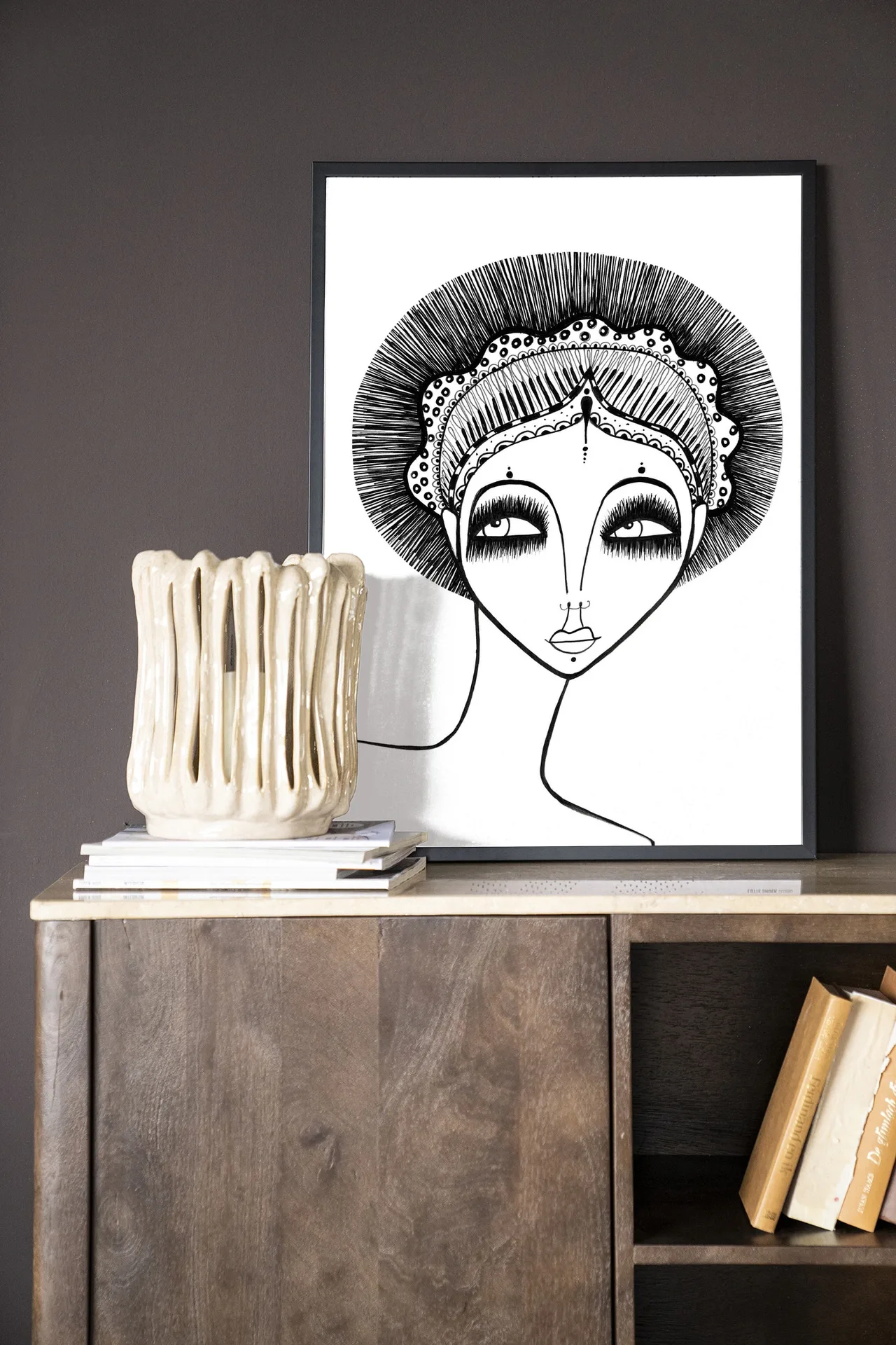 Wandkleed Leyla - Urban Cotton in een lijst, staand op een houten dressoir met boeken