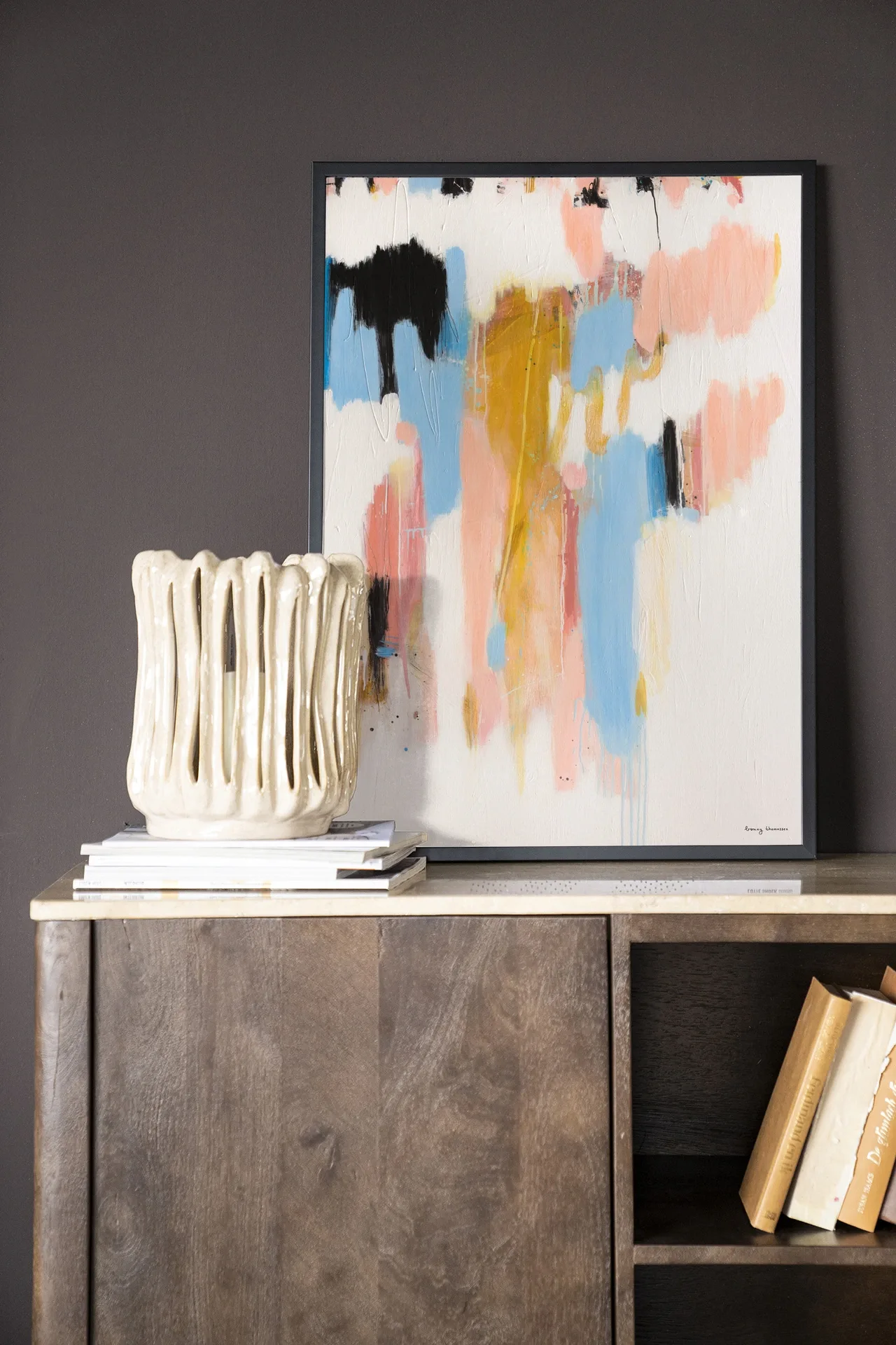 Wandkleed Better Days - Urban Cotton hangend boven een houten dressoir met boeken en een vaas