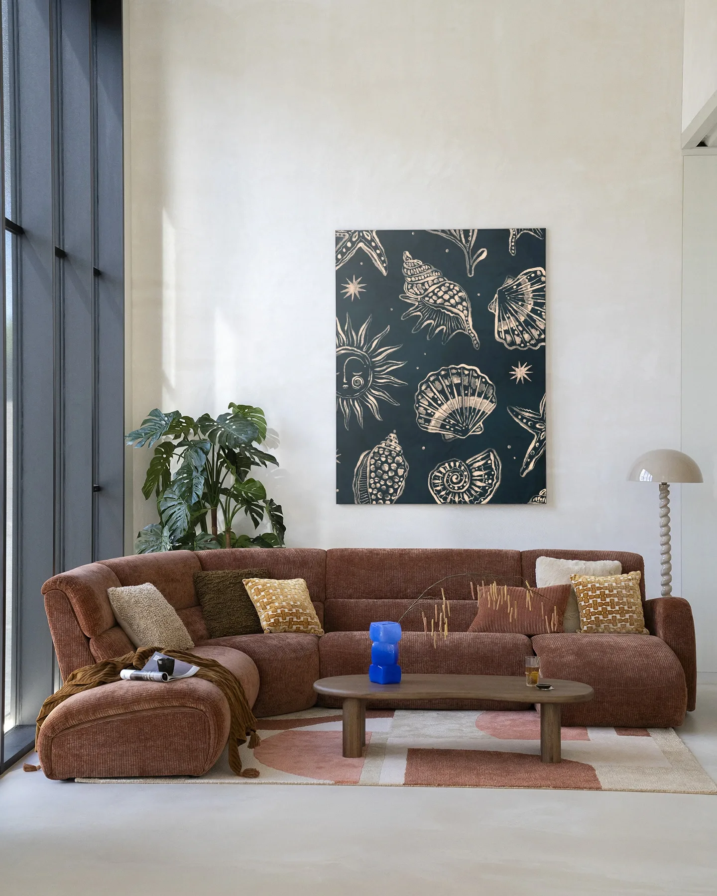 Het Wandkleed Seashells Midnight - Urban Cotton hangt boven een bruine bank in een lichte woonkamer