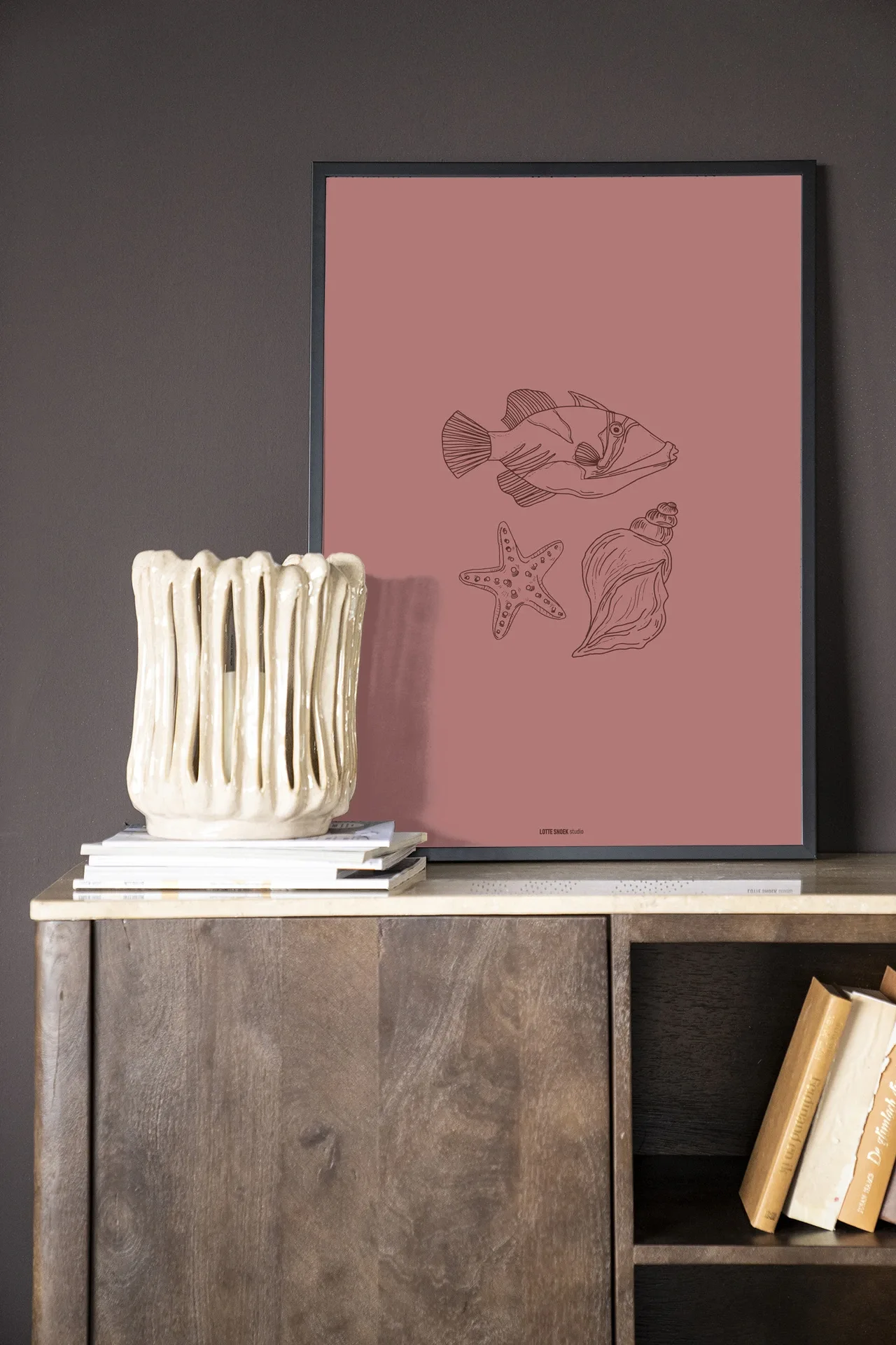 Wandkleed Tres Pisces - Urban Cotton in een lijst, staand op een houten dressoir met een vaas en boeken