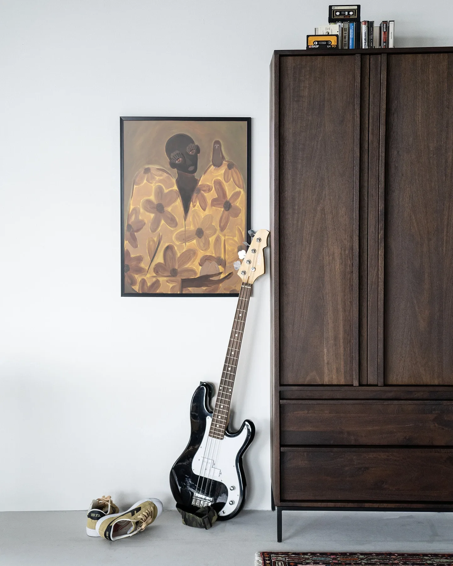 Wandkleed Twins - Urban Cotton hangt aan een witte muur naast een donkerbruine kast, met een basgitaar en schoenen op de vloer