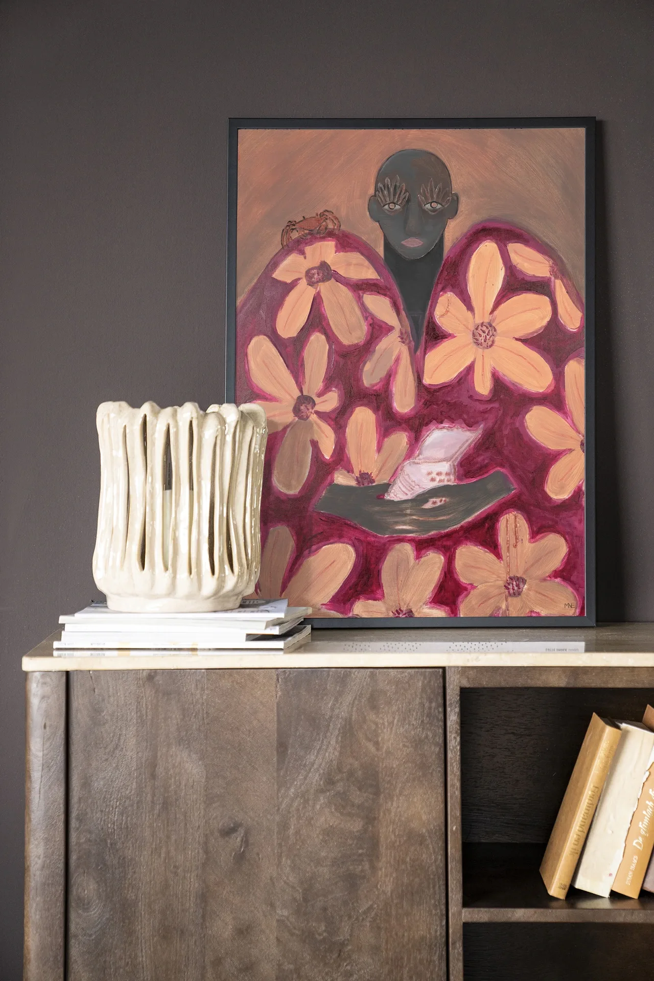 Wandkleed Borrowed Home - Urban Cotton in een lijst, staand op een houten dressoir met boeken