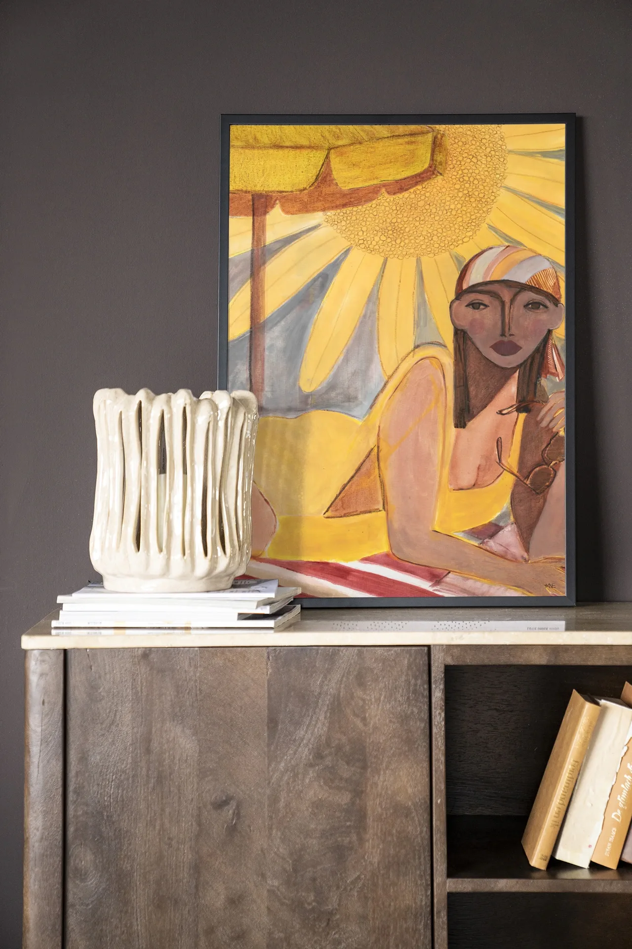 Wandkleed Sunflower Sun - Urban Cotton hangt boven een houten dressoir met een vaas en boeken