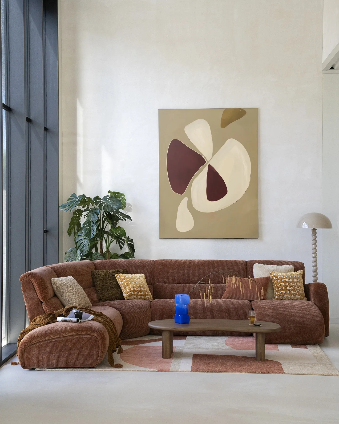 Wandkleed Elegant - Urban Cotton hangt boven een bruine ribfluwelen hoekbank in een lichte woonkamer