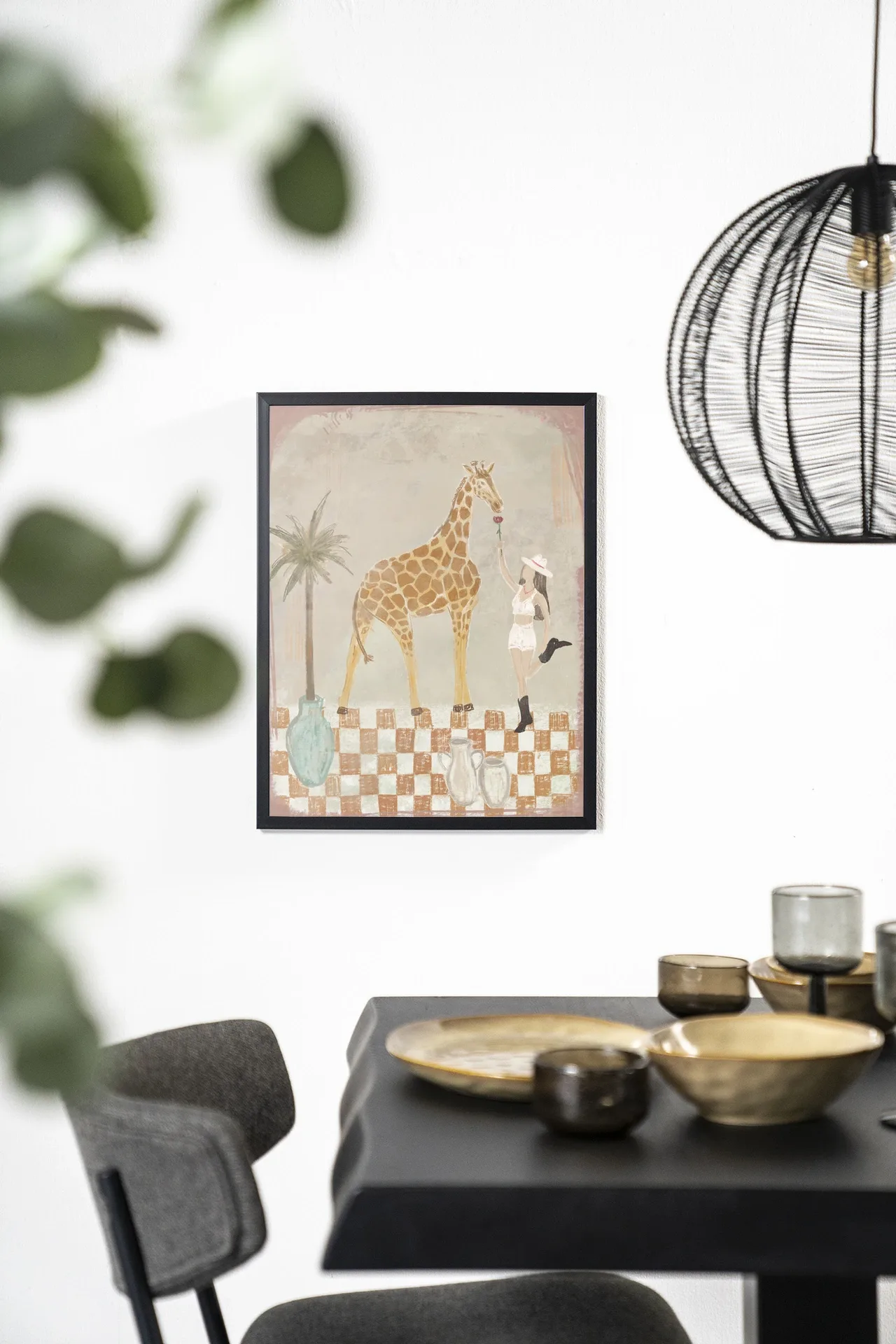 Wandkleed Feeding Rose, ingelijst aan een witte muur boven een zwarte tafel met gouden servies - Urban Cotton