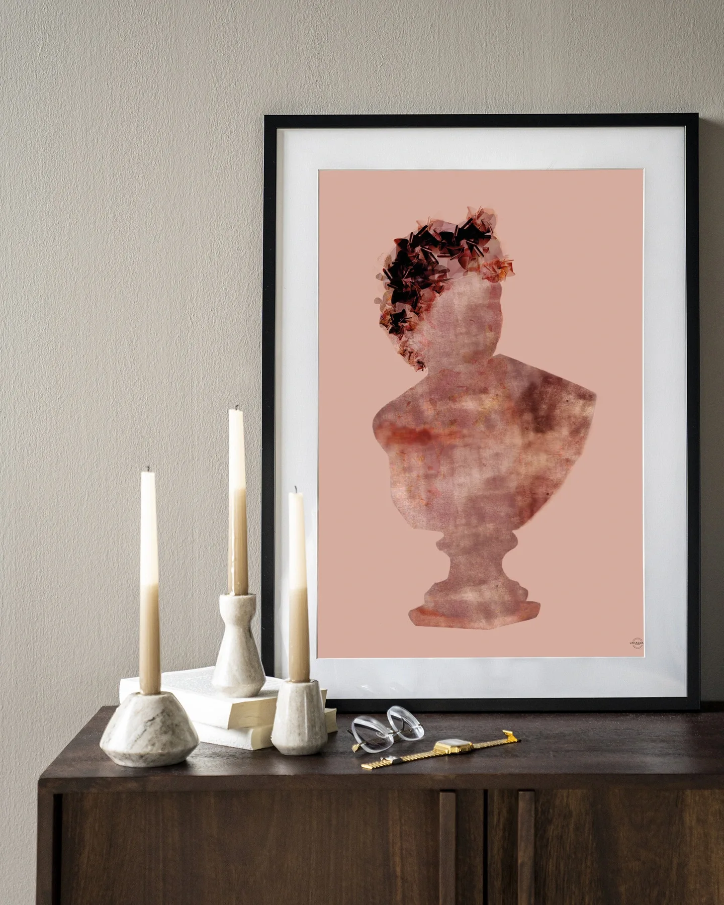 Art print Eroded Roman Sculpture - Urban Cotton in een lijst, staand op een donkerbruin dressoir met kaarsen en boeken