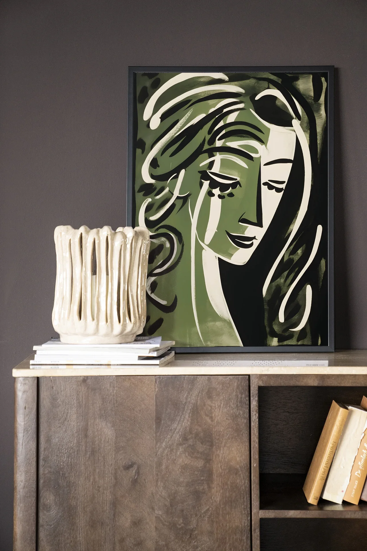 Wandkleed Aphrodite - Urban Cotton in een lijst, staand op een houten dressoir met boeken