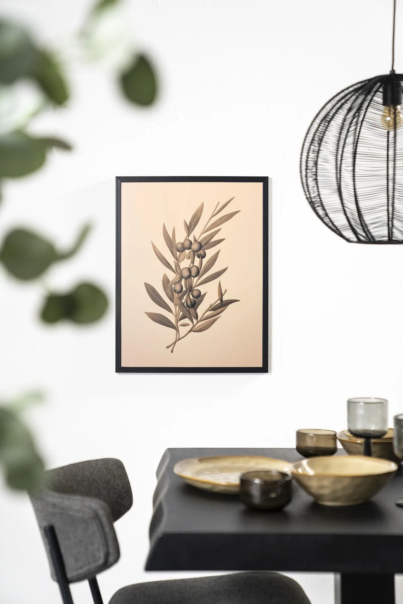 Wandkleed Oliva met een olijftak, hangend aan een witte muur boven een zwarte tafel - Urban Cotton