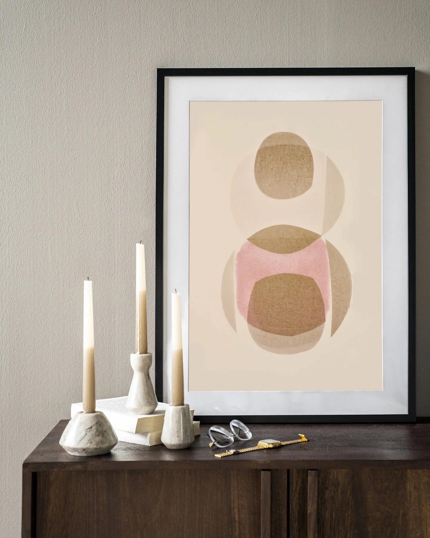 Art print Figuras 3 - Urban Cotton in een zwarte lijst, staand op een donkerbruine houten kast met kaarsen en een bril