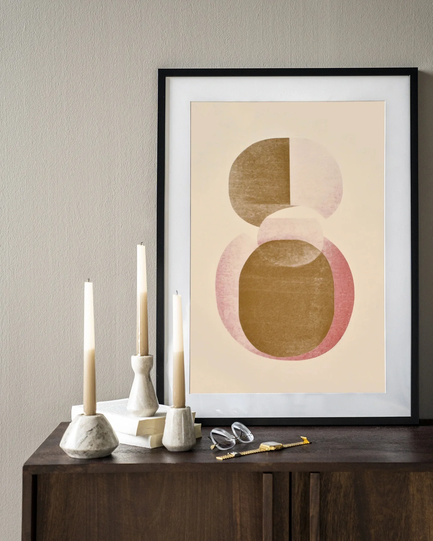 De Art print Figuras 4 - Urban Cotton hangt in een zwarte lijst boven een houten dressoir met kaarsen en boeken