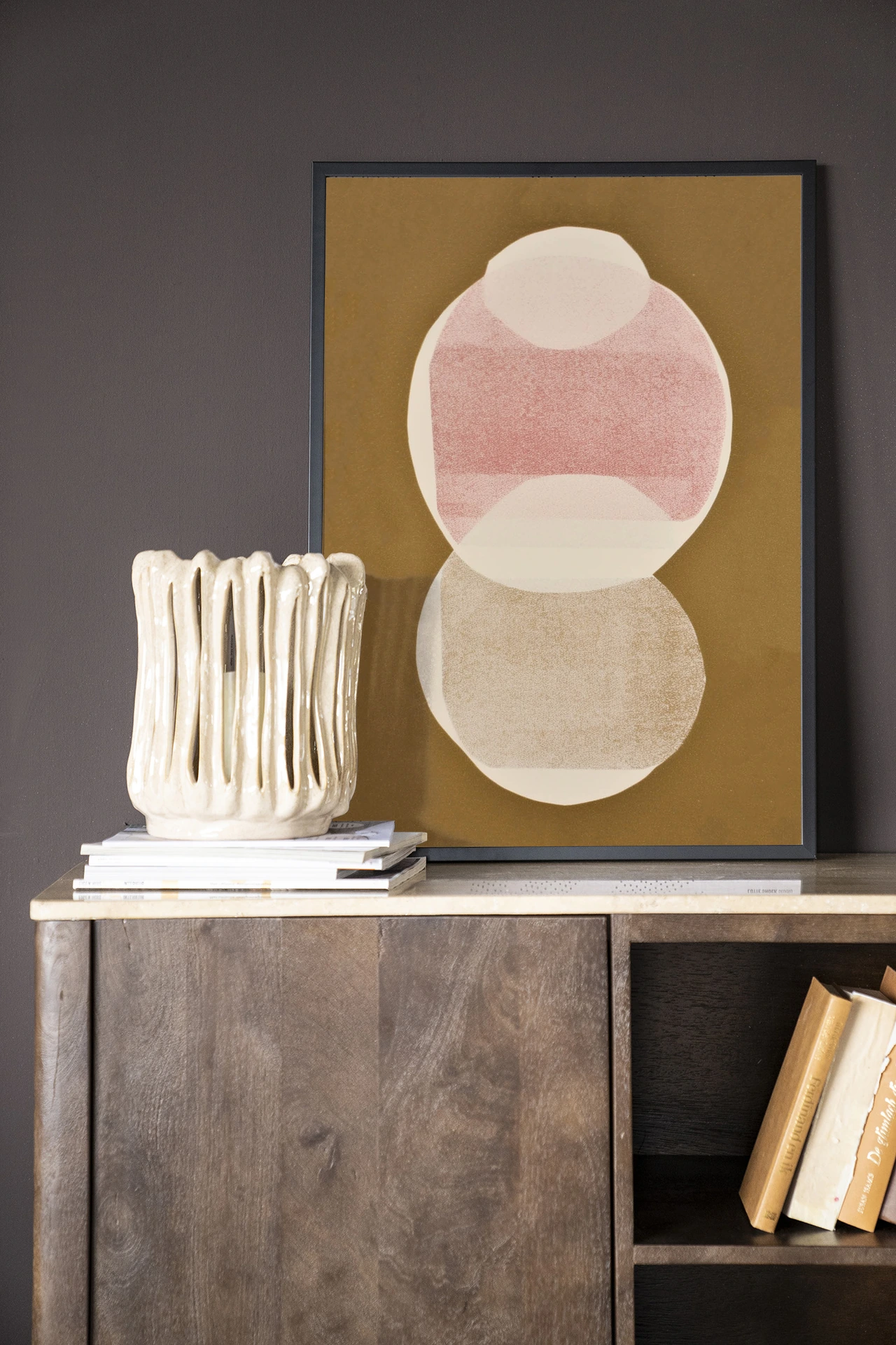 De Art print Figuras 6 - Urban Cotton staat op een houten dressoir met een vaas en boeken