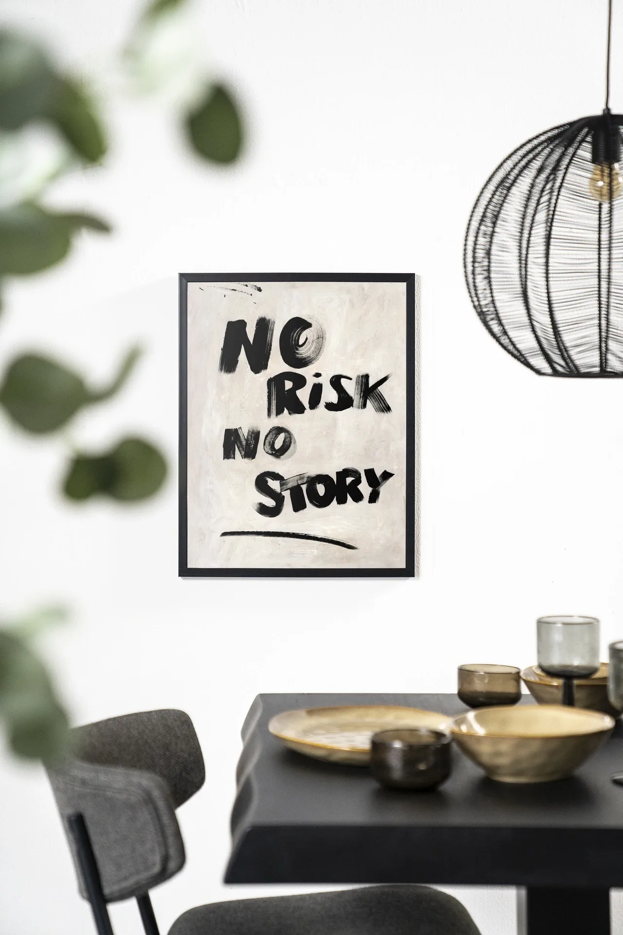 Wandkleed No Risk, No Story hangt aan een witte muur boven een zwarte eettafel met gouden schalen - Urban Cotton