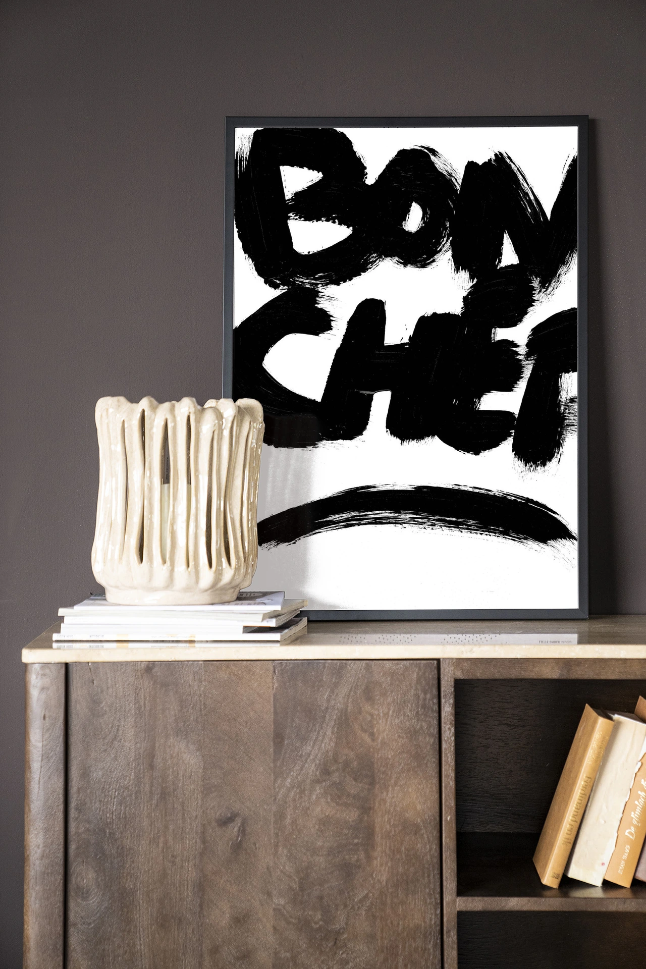 Wandkleed Bon Chef - Urban Cotton in een zwarte lijst, staand op een houten dressoir met een crèmekleurige vaas