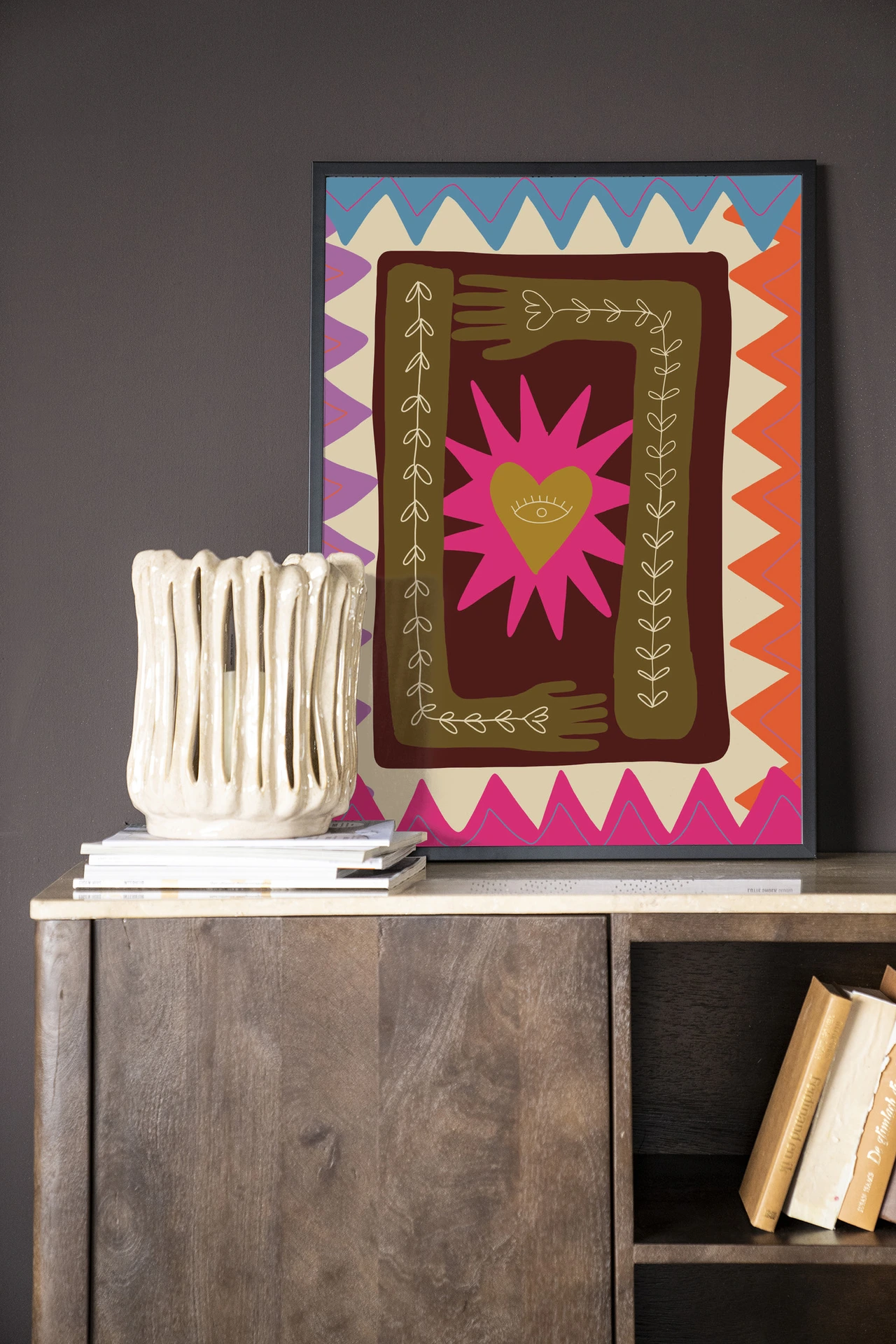 Wandkleed Hug - Urban Cotton aan een donkere muur, met een vaas en boeken op een houten kast eronder