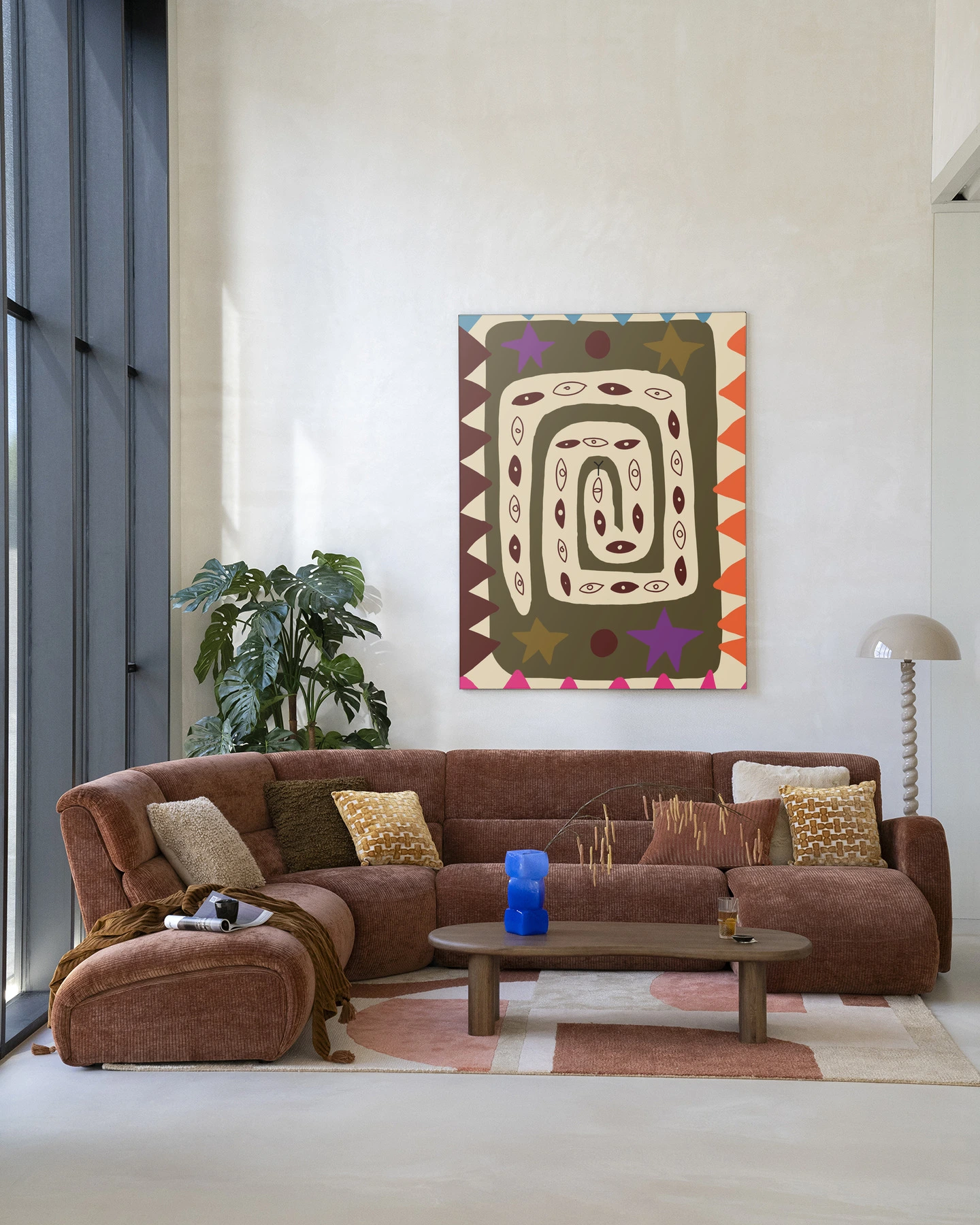 Wandkleed Snake Eye - Urban Cotton hangt boven een bruine ribfluwelen bank in een lichte woonkamer
