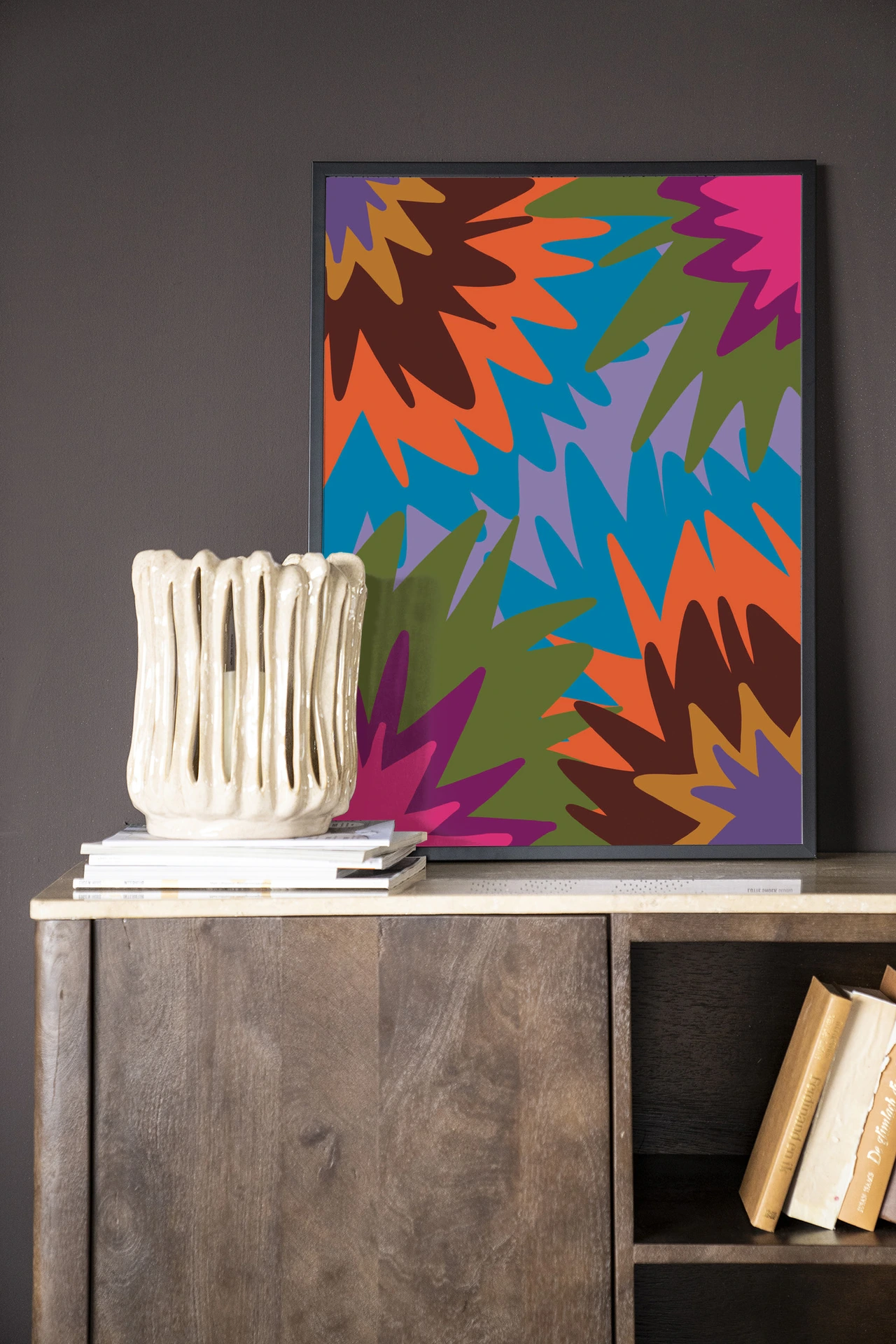 Wandkleed Fireworks van Urban Cotton in een lijst, staand op een houten dressoir met boeken