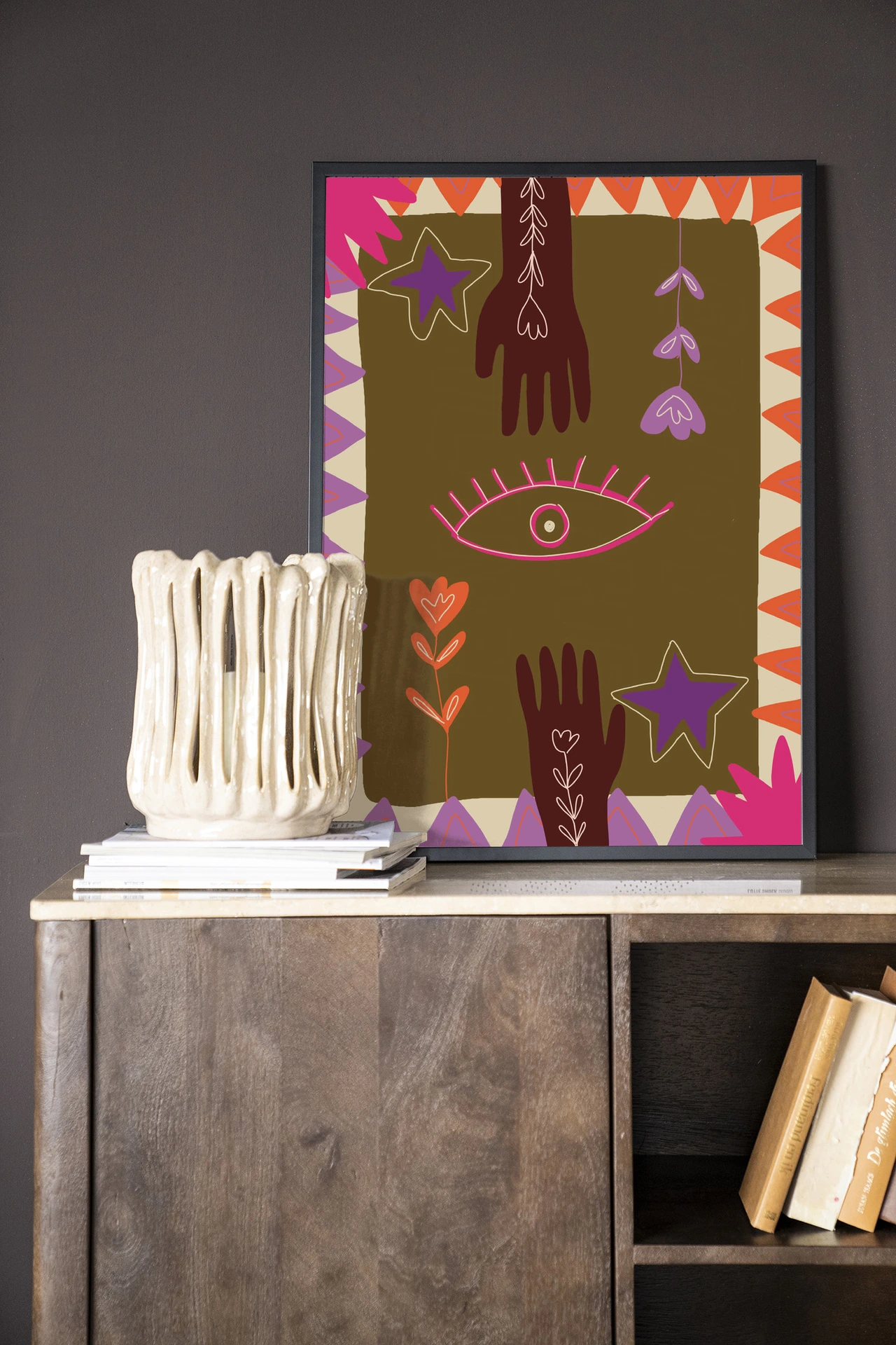 Wandkleed Hands - Urban Cotton hangt aan een donkere muur boven een houten dressoir met boeken