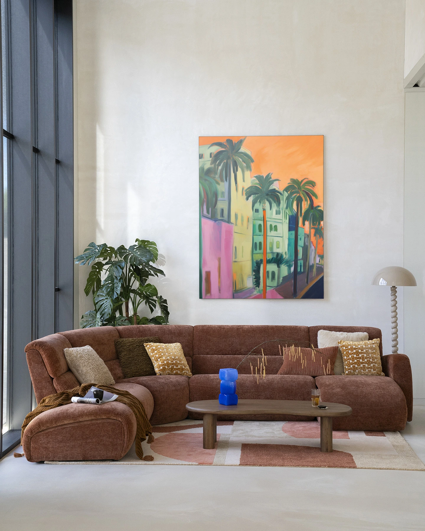 Wandkleed Palm Street - Urban Cotton hangt boven een bruine bank in een lichte woonkamer