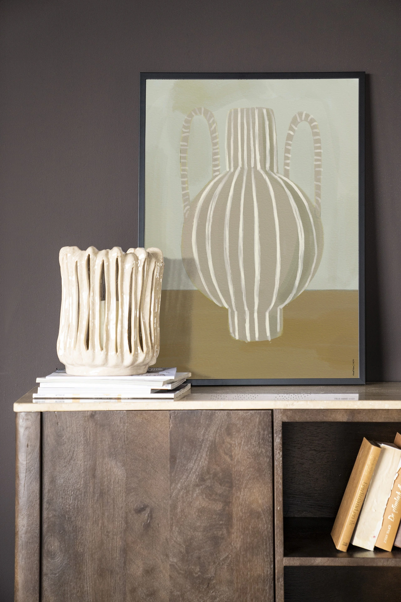 Wandkleed Vivid Vase 04 - Urban Cotton hangend boven een houten dressoir met boeken en een vaas