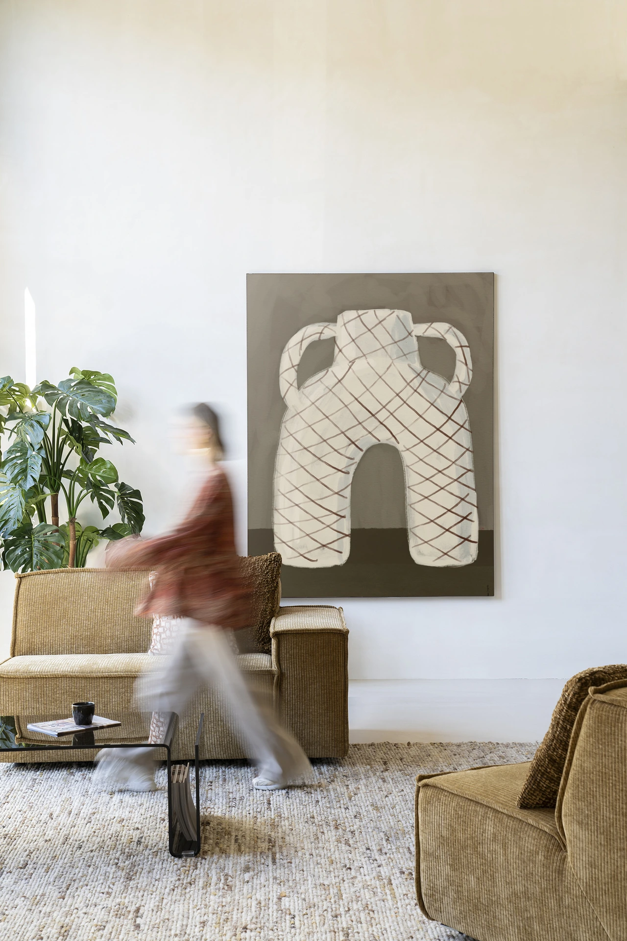 Een levendige woonkamer met het Wandkleed Vivid Vase 05 - Urban Cotton aan een witte muur, een bank en een persoon in beweging