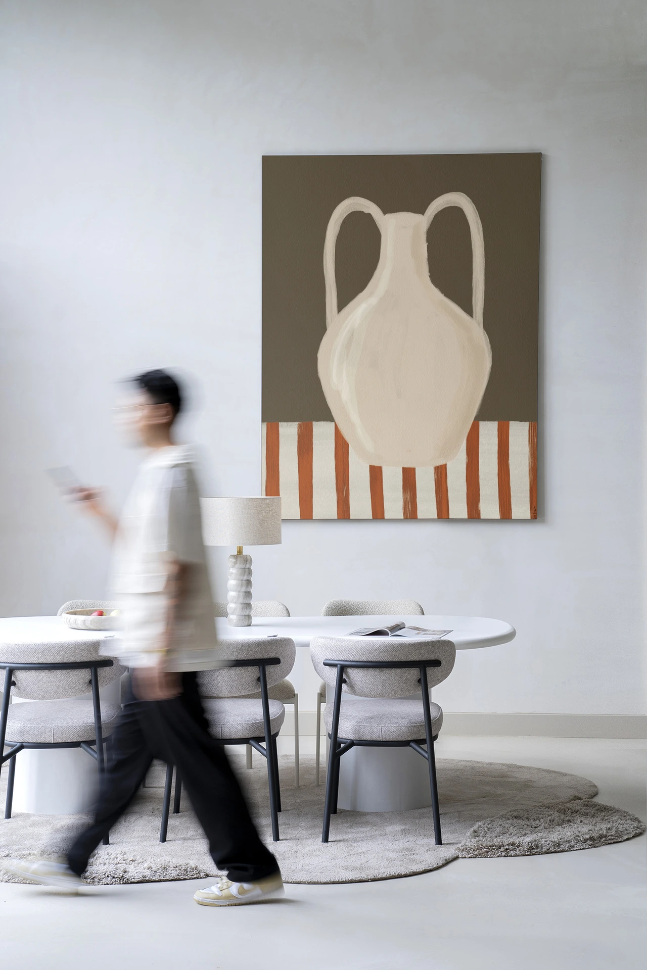 Een man loopt langs een eettafel met stoelen en een Wandkleed Vivid Vase 06 - Urban Cotton aan de muur