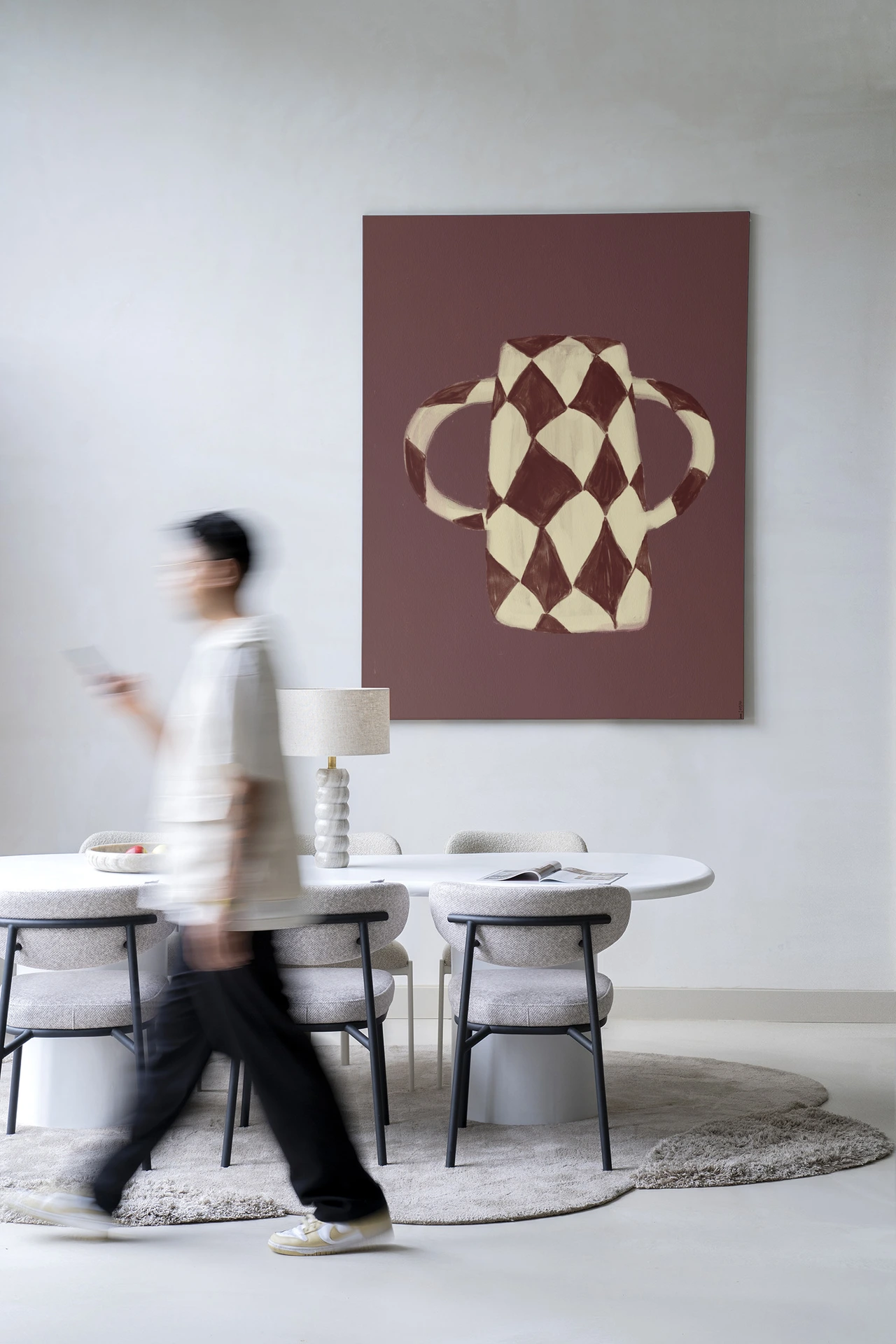 Een persoon loopt langs een witte eettafel met stoelen en een Wandkleed Vivid Vase 07 - Urban Cotton aan de muur