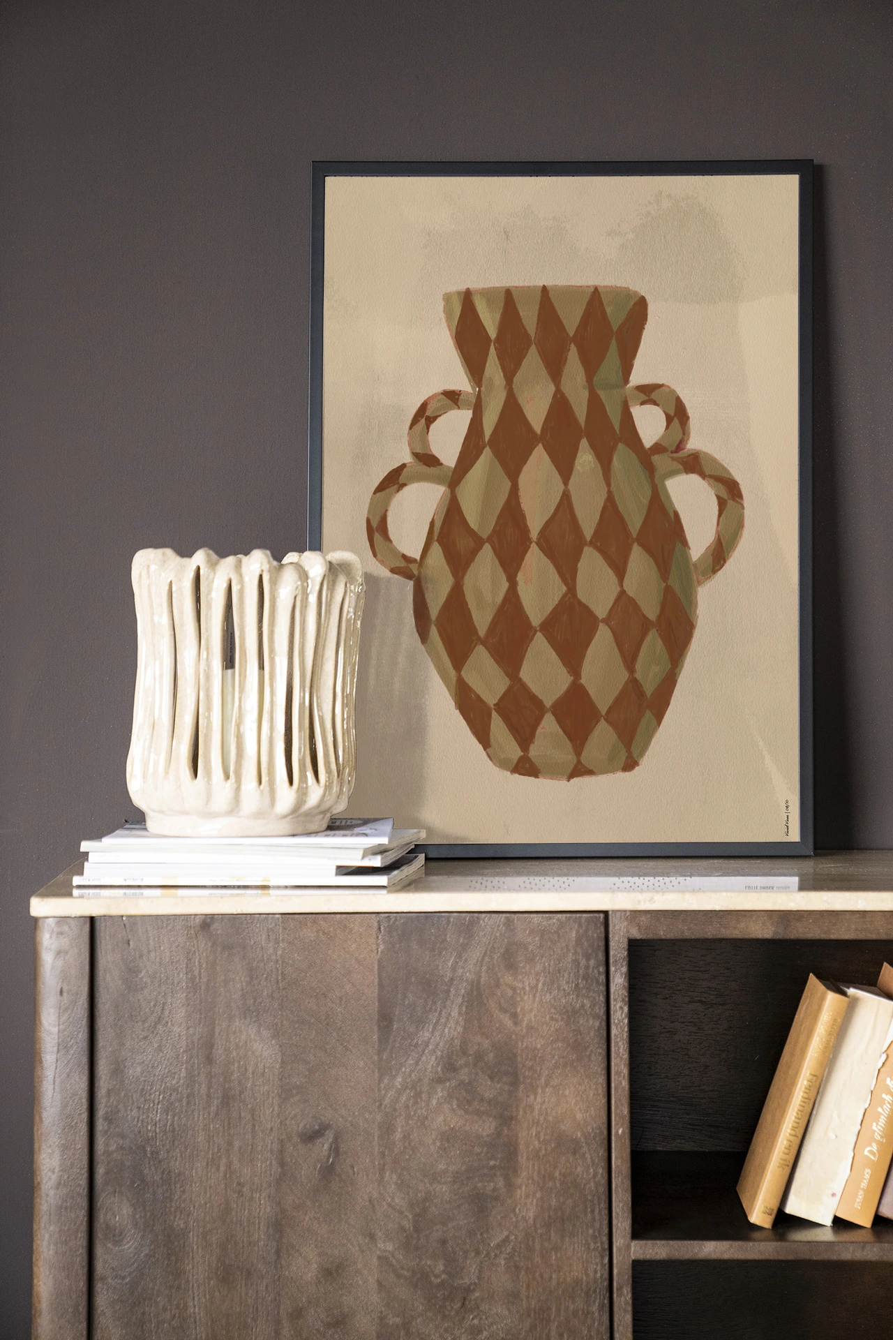 Wandkleed Vivid Vase 08 - Urban Cotton hangt boven een houten dressoir met boeken en een witte vaas